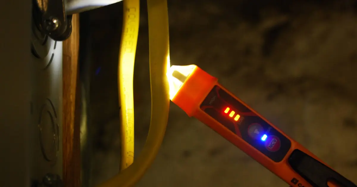 A hand holding a non-contact voltage tester near a metal pressure switch housing next to a well pressure tank in a basement utility area