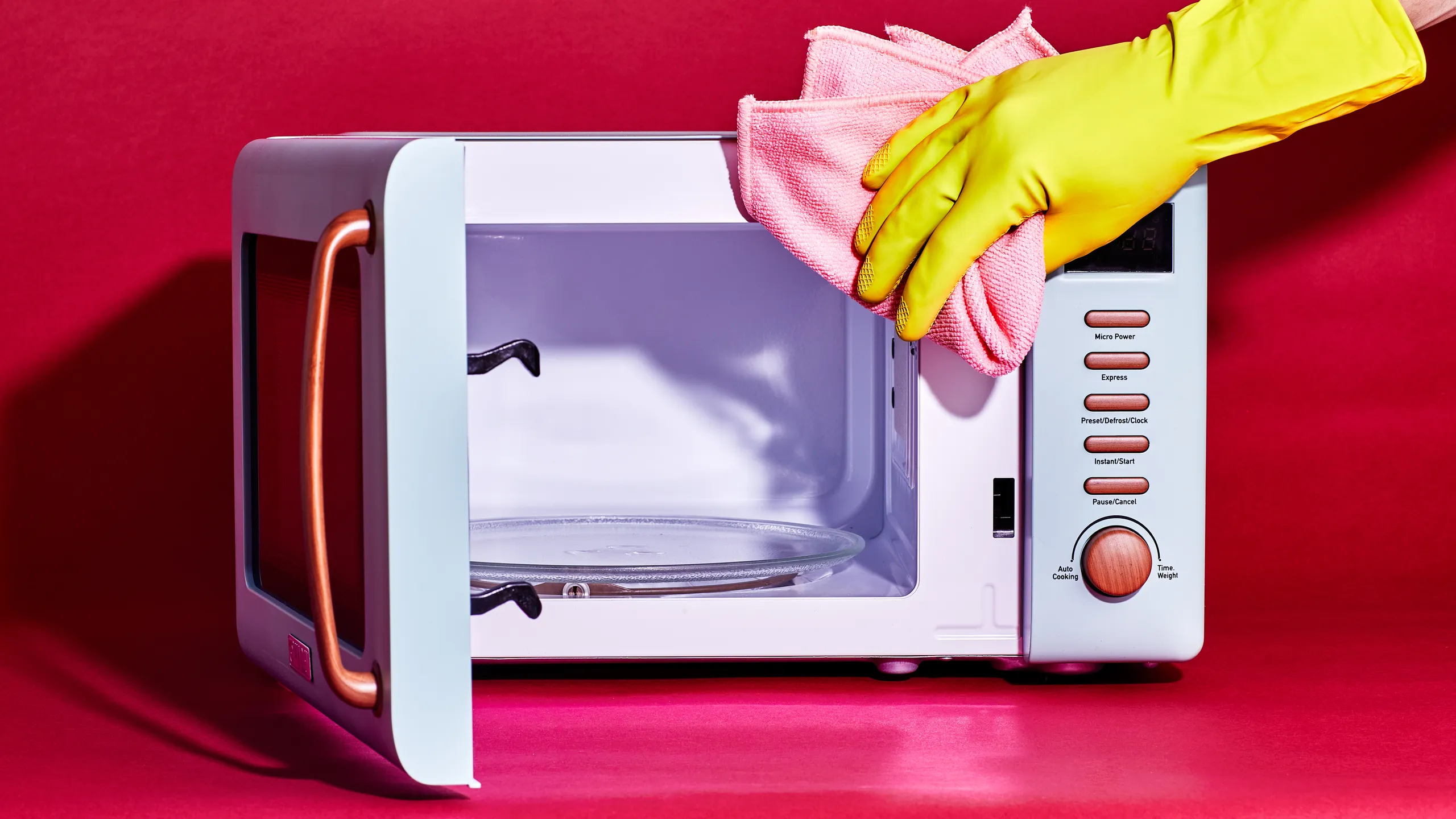 A hand wiping the inside ceiling of a microwave with a damp microfiber cloth, focusing on greasy splatter spots