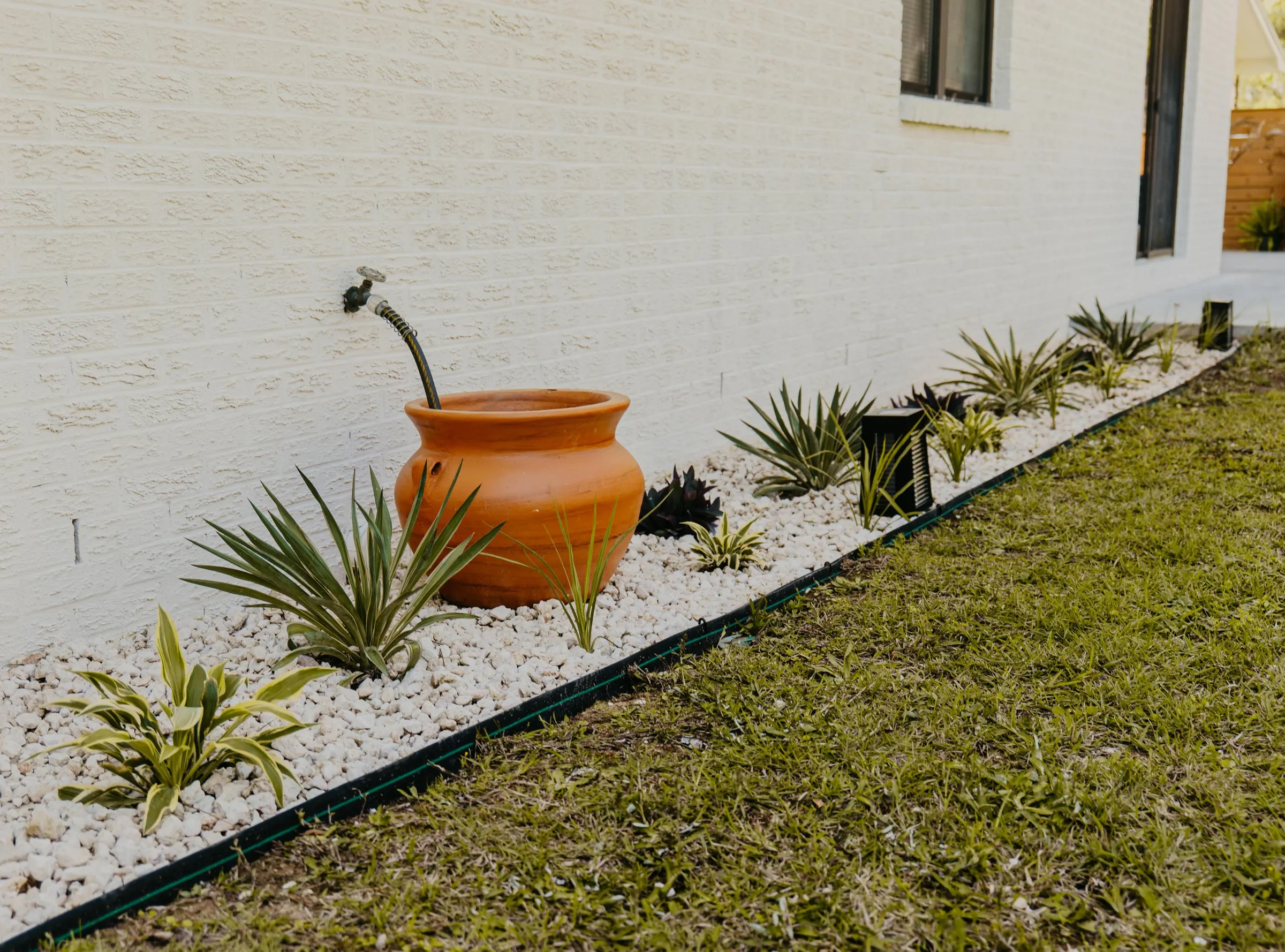 A home exterior with a neat gravel border along the foundation, trimmed shrubs, and a clean mulch bed set back from the wall, realistic daytime photo