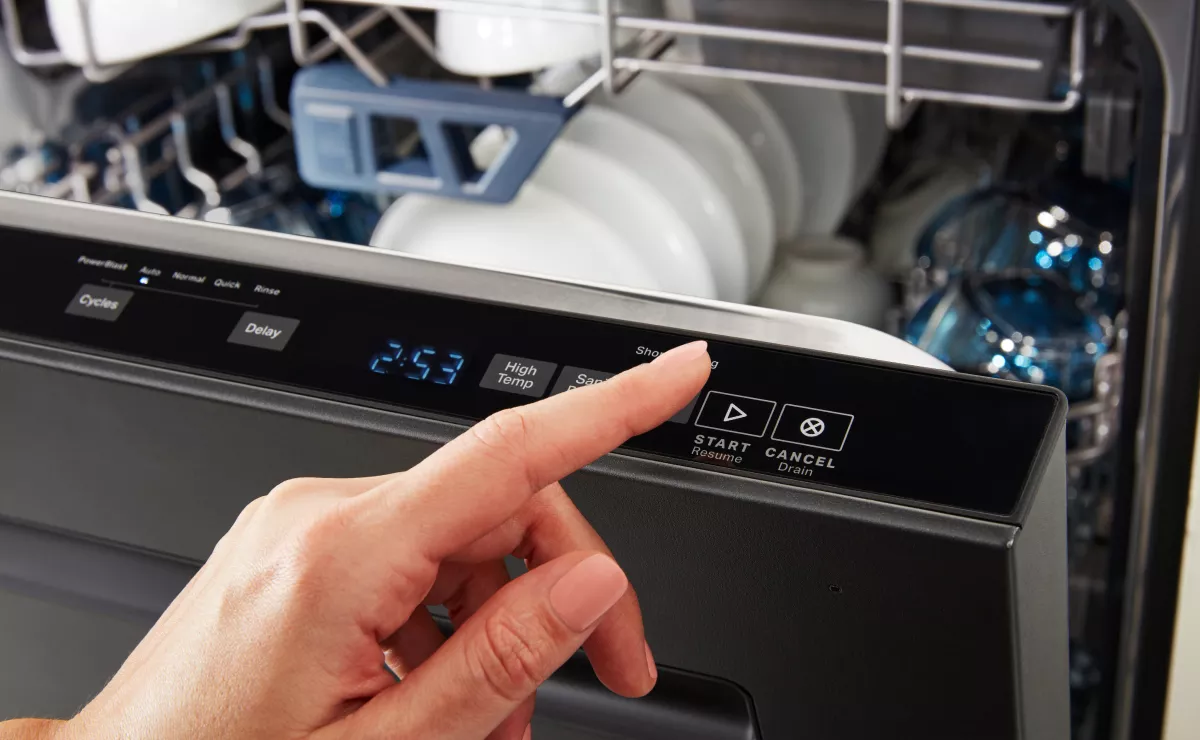 A homeowner hand pressing a cancel or drain button on a dishwasher control panel in a normal kitchen, close-up photo