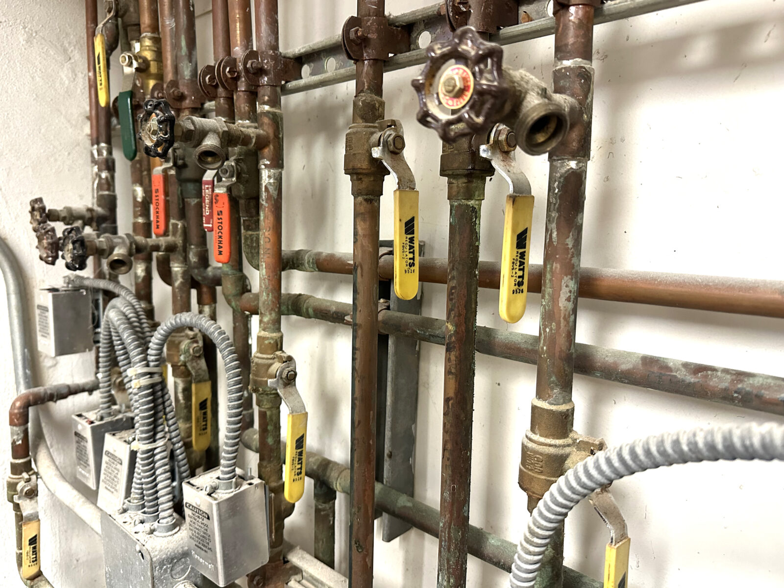 A homeowner hand turning a dedicated irrigation shutoff ball valve on a copper pipe in a basement utility area