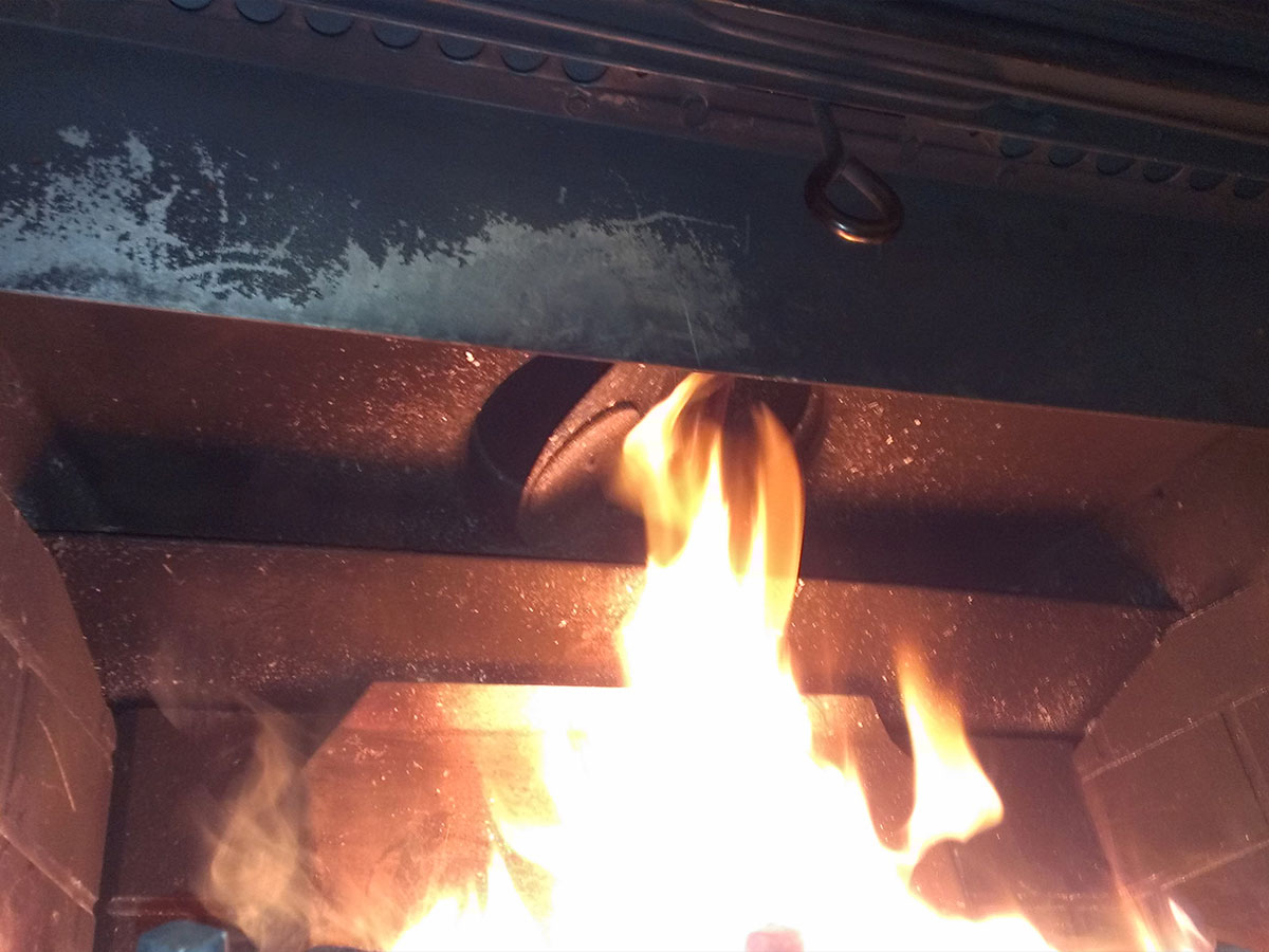 A homeowner kneeling in front of a wood-burning fireplace using a flashlight to look up into the throat and verify the damper is open, realistic indoor photo