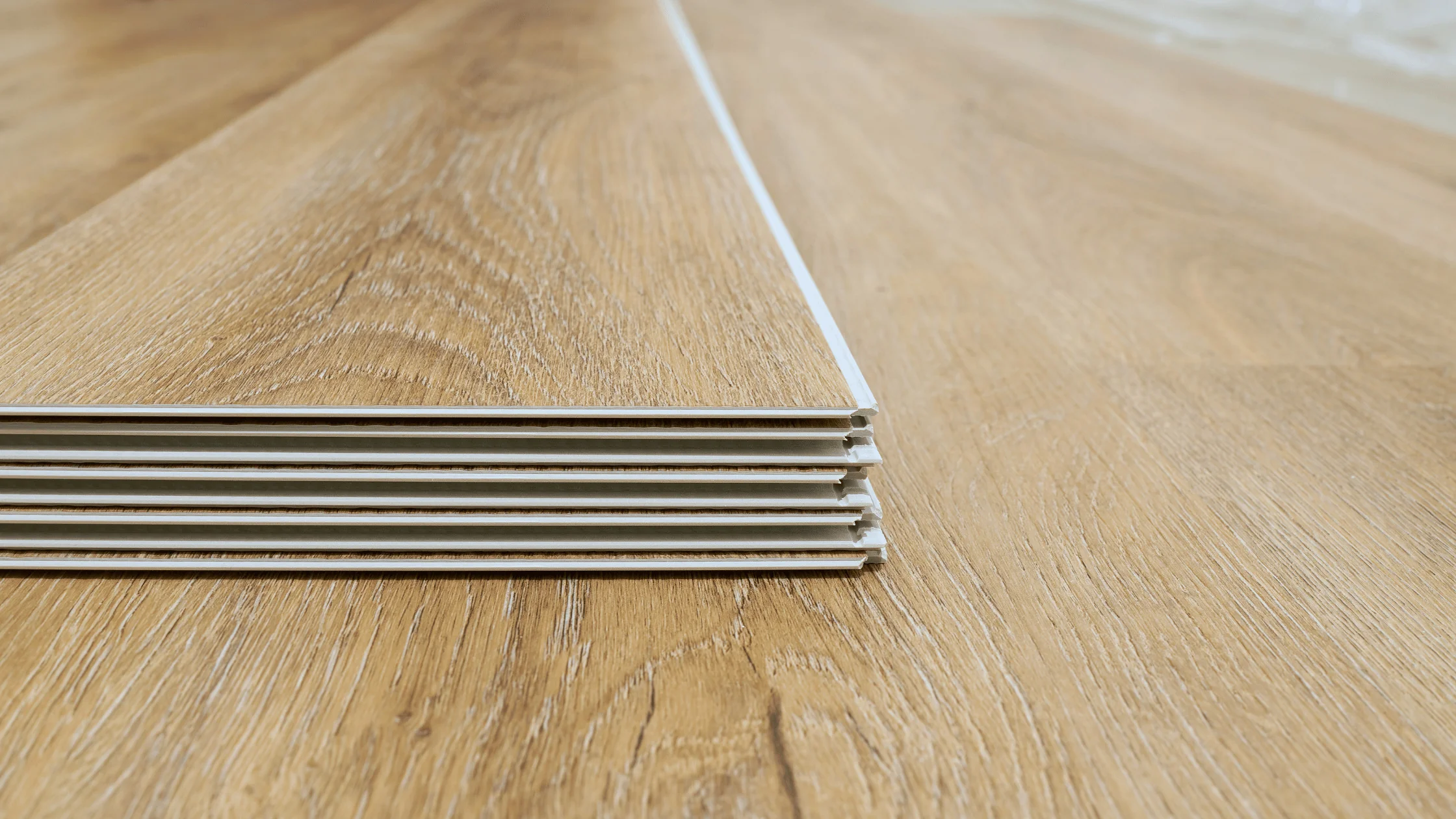 A homeowner kneeling on a plywood subfloor while snapping click-lock vinyl planks together in a bright, empty room