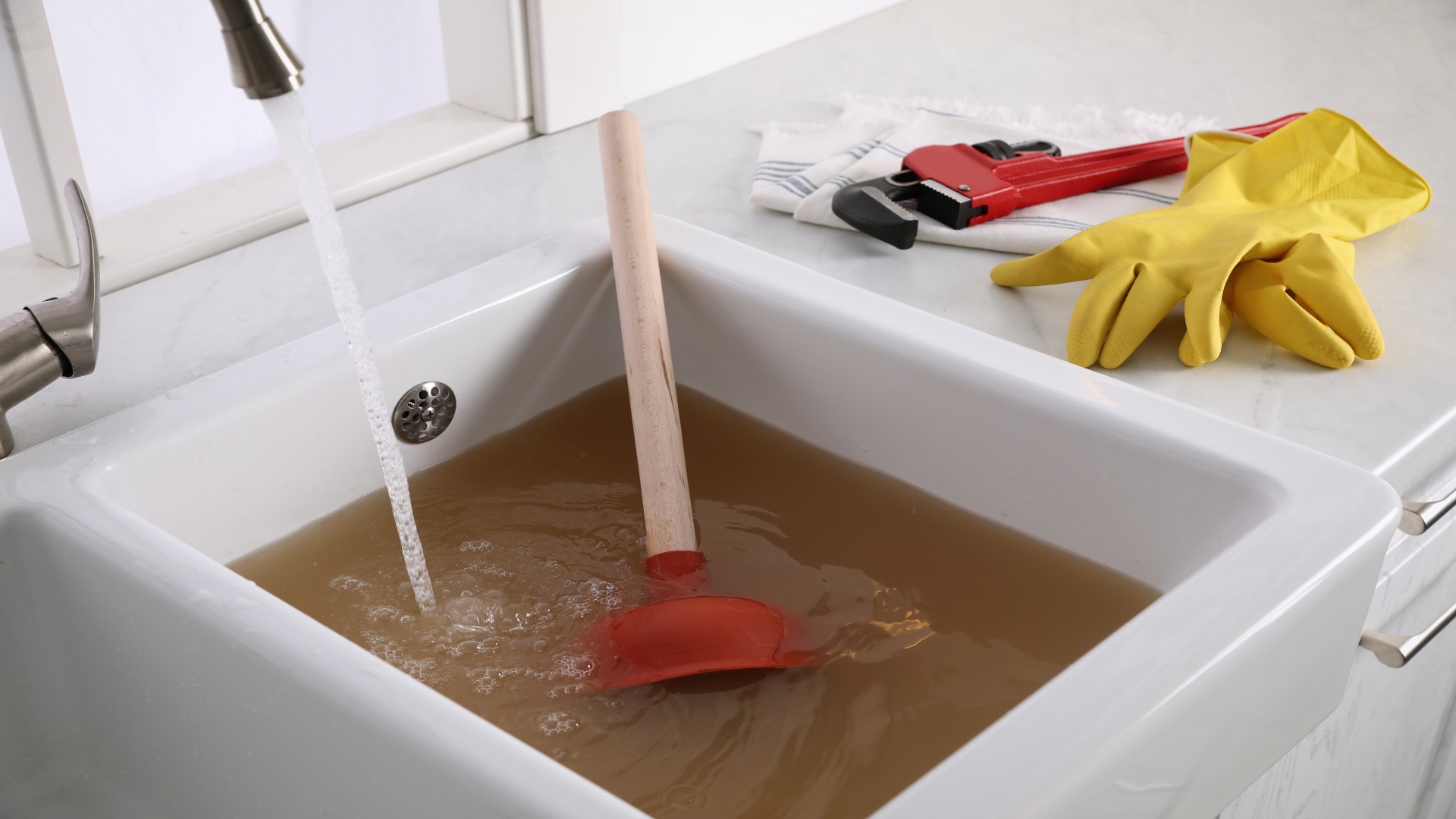 A homeowner plunging a kitchen sink with a cup plunger while a few inches of water sit in the basin, real-life home repair photo