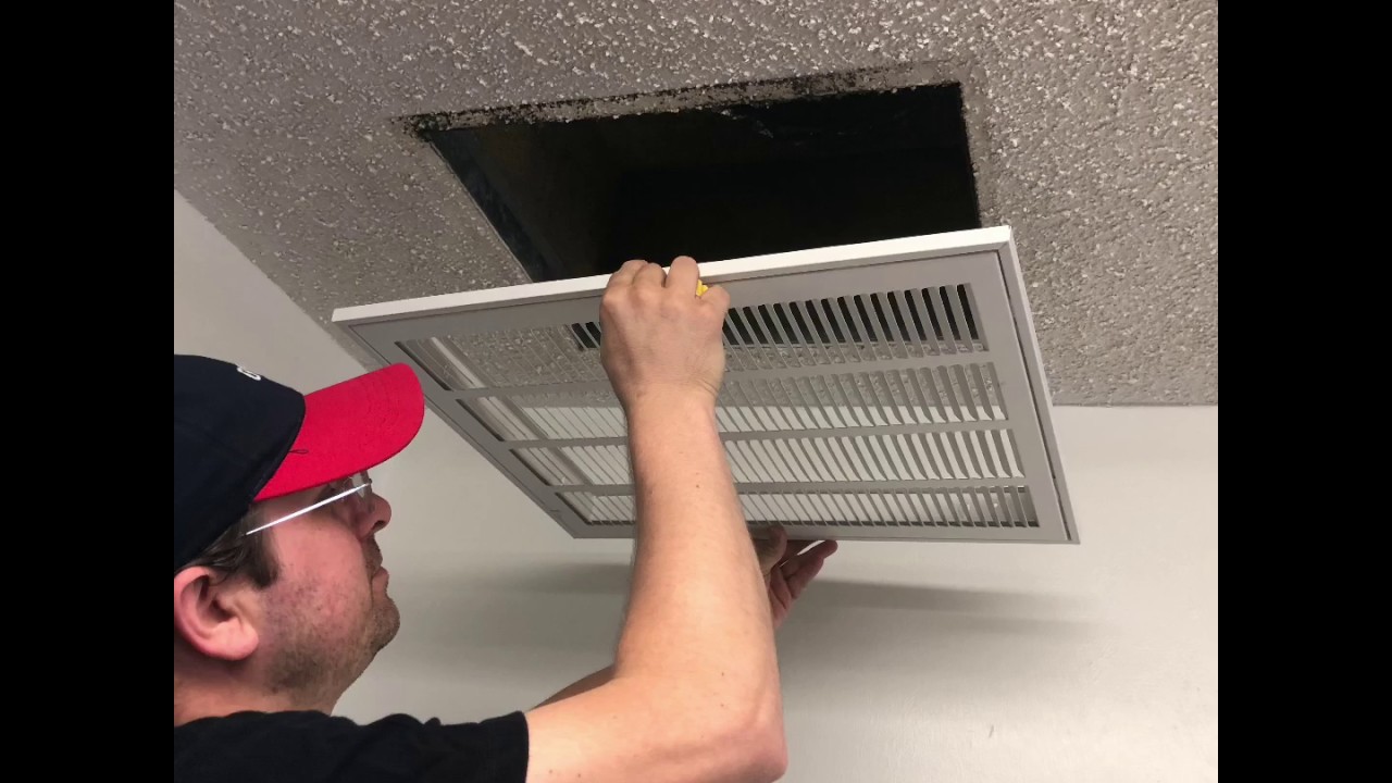 A homeowner sliding a pleated HVAC air filter into a return grille, close-up realistic home photo