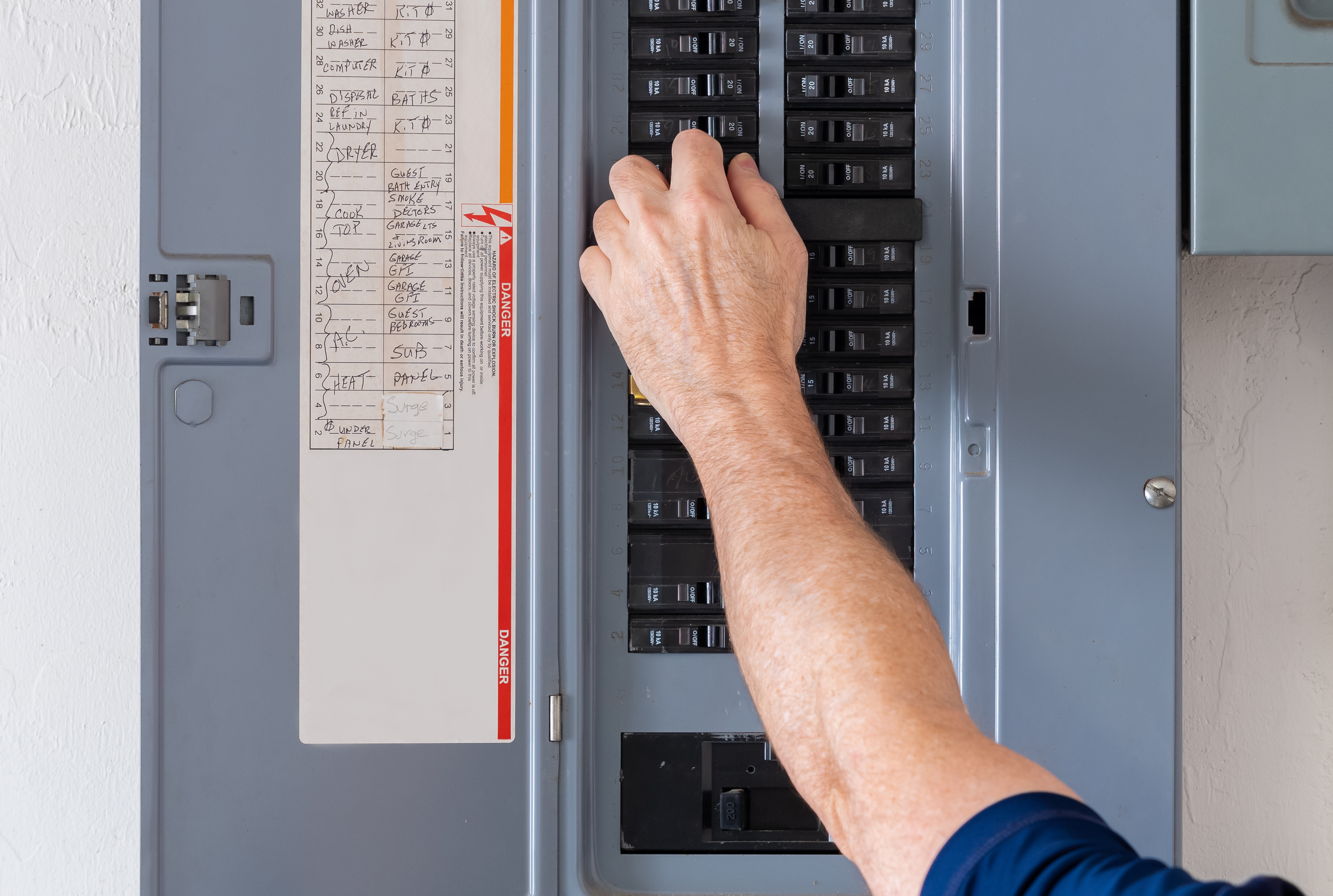A homeowner standing at an open residential breaker panel in a garage, hand near the breakers, real photo