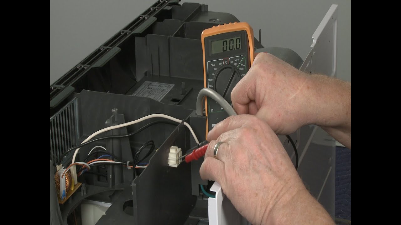 A homeowner using a multimeter to test wiring connectors near an over-the-range microwave vent fan motor with the unit unplugged