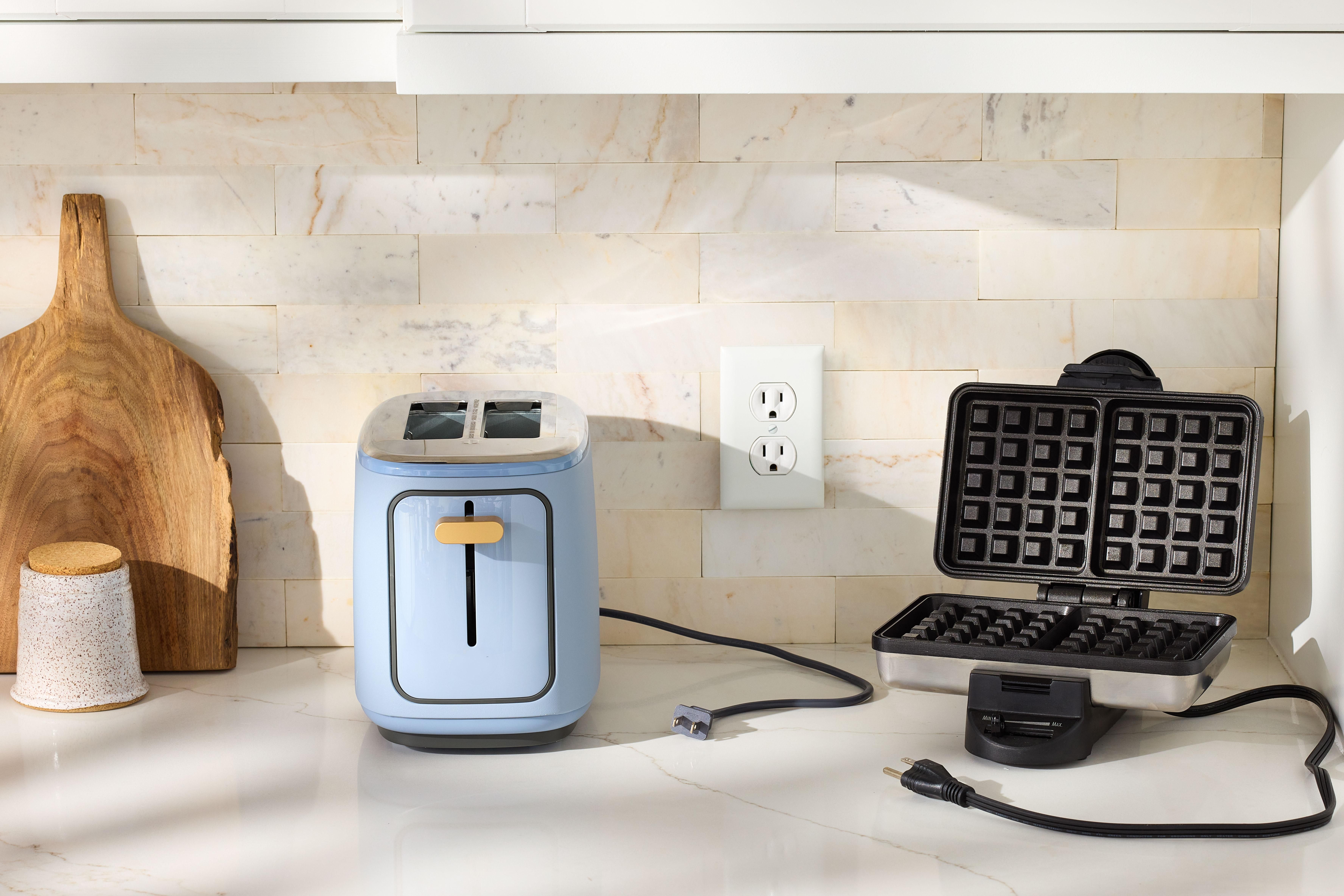 A kitchen countertop with a toaster, electric kettle, and coffee maker plugged into outlets, cords visible and neatly routed, realistic home photo