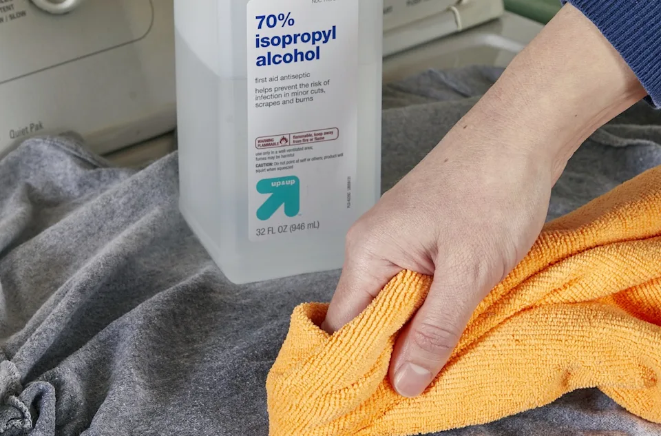 A microfiber cloth, a small bottle of isopropyl alcohol, and a bowl of soapy water on a kitchen counter ready for cleaning