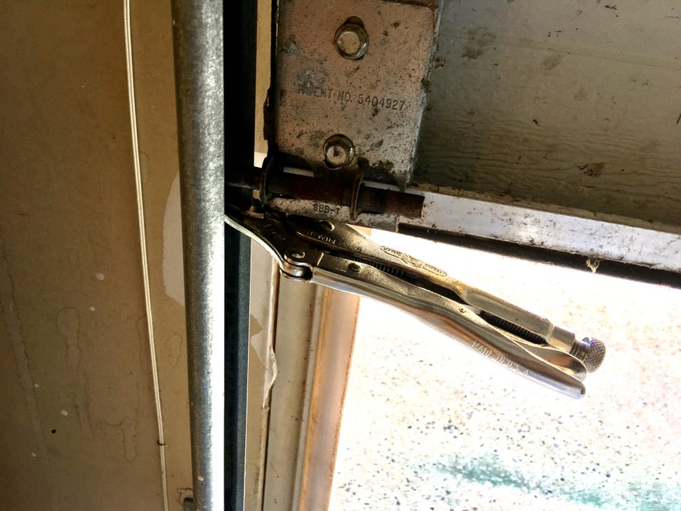 A pair of locking pliers clamped to a metal garage door track just above a roller to prevent the door from moving, photographed inside a home garage