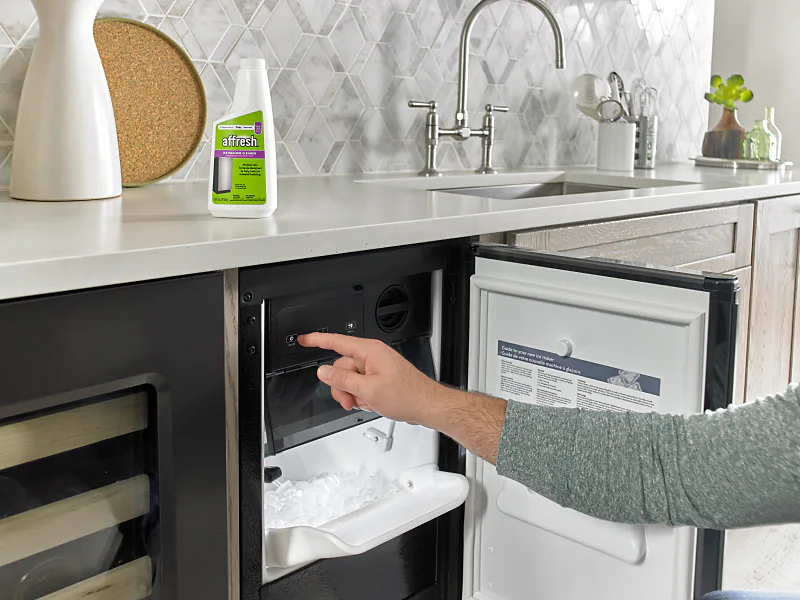 A person washing a refrigerator ice bin in a kitchen sink with warm soapy water, real photo