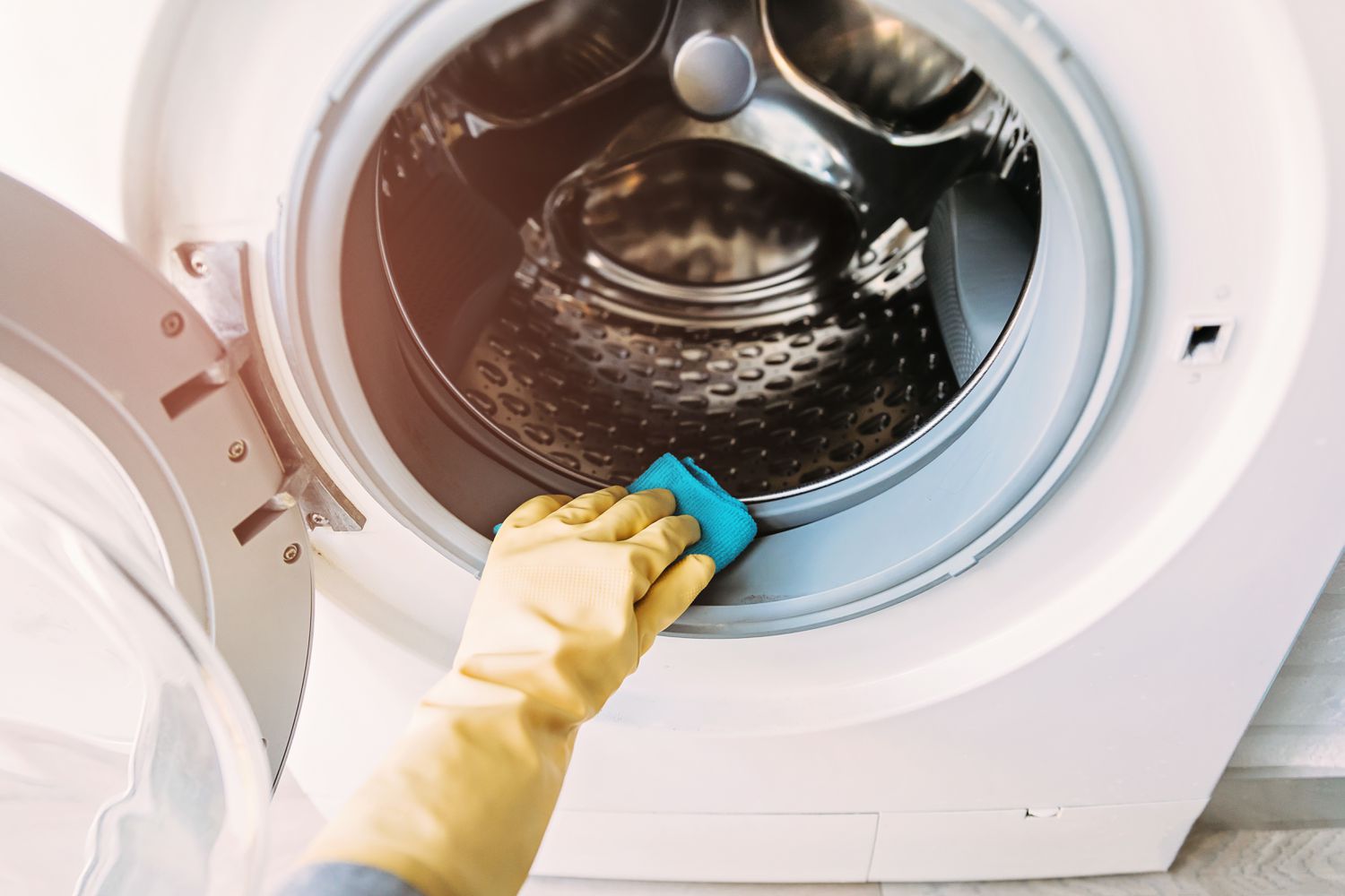 A person wiping the rubber door gasket of a front-loading washing machine with a microfiber cloth, close-up photo