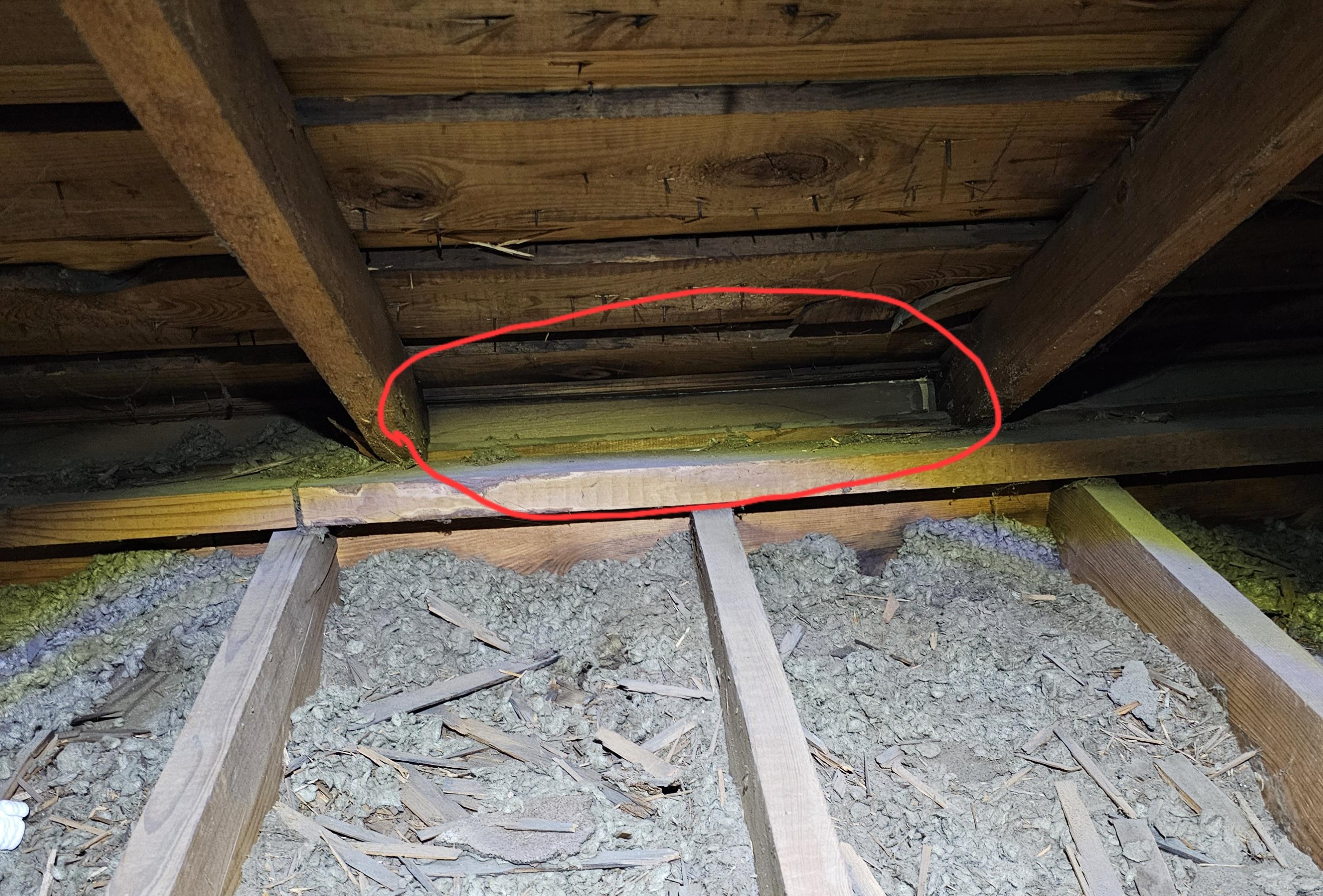 A photo in an attic at the eaves where insulation is packed tight against the roof deck, blocking soffit airflow with no baffle installed