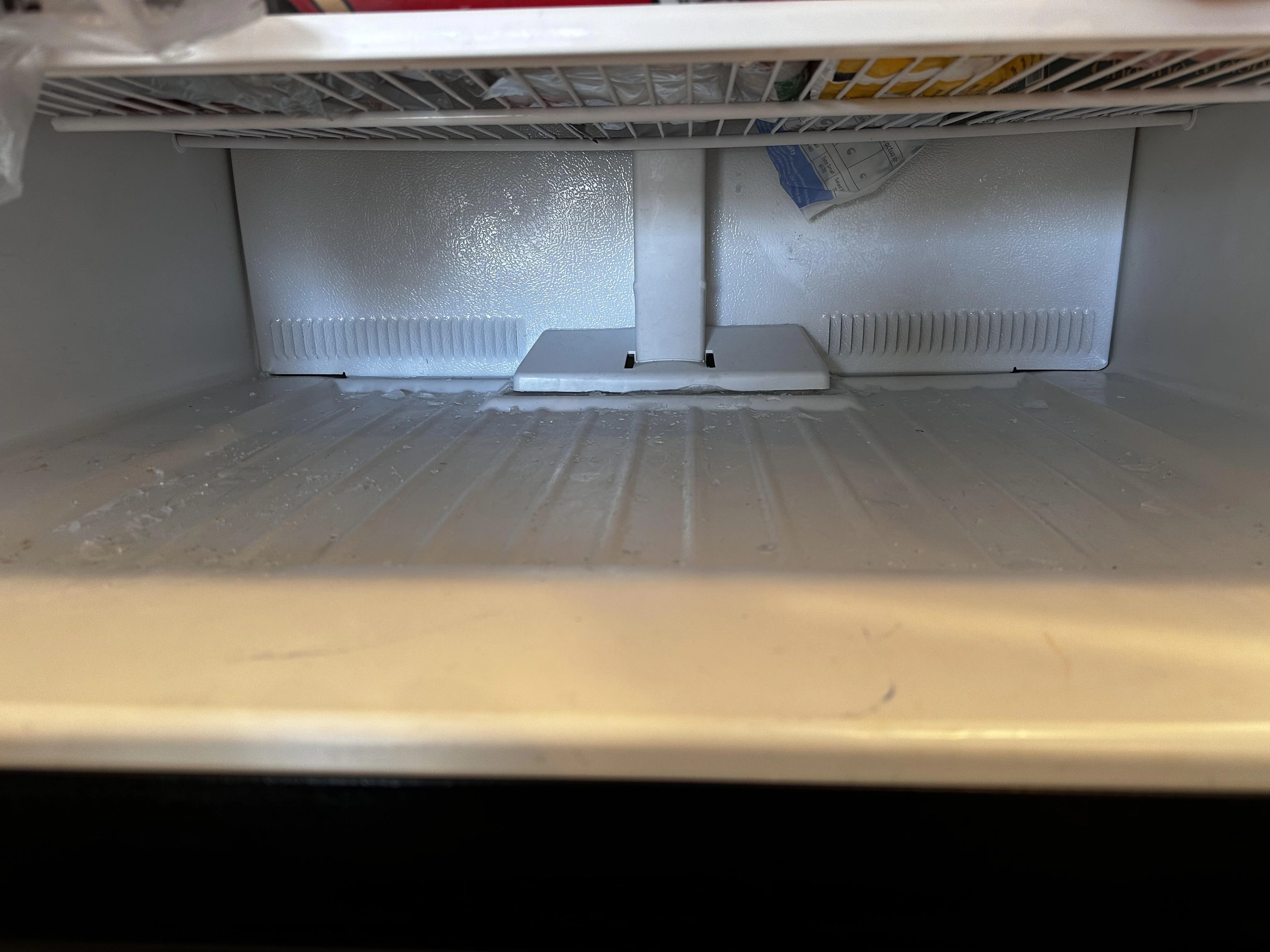 A photo inside a freezer showing a thin sheet of ice across the bottom floor near the drain area, realistic home appliance scene