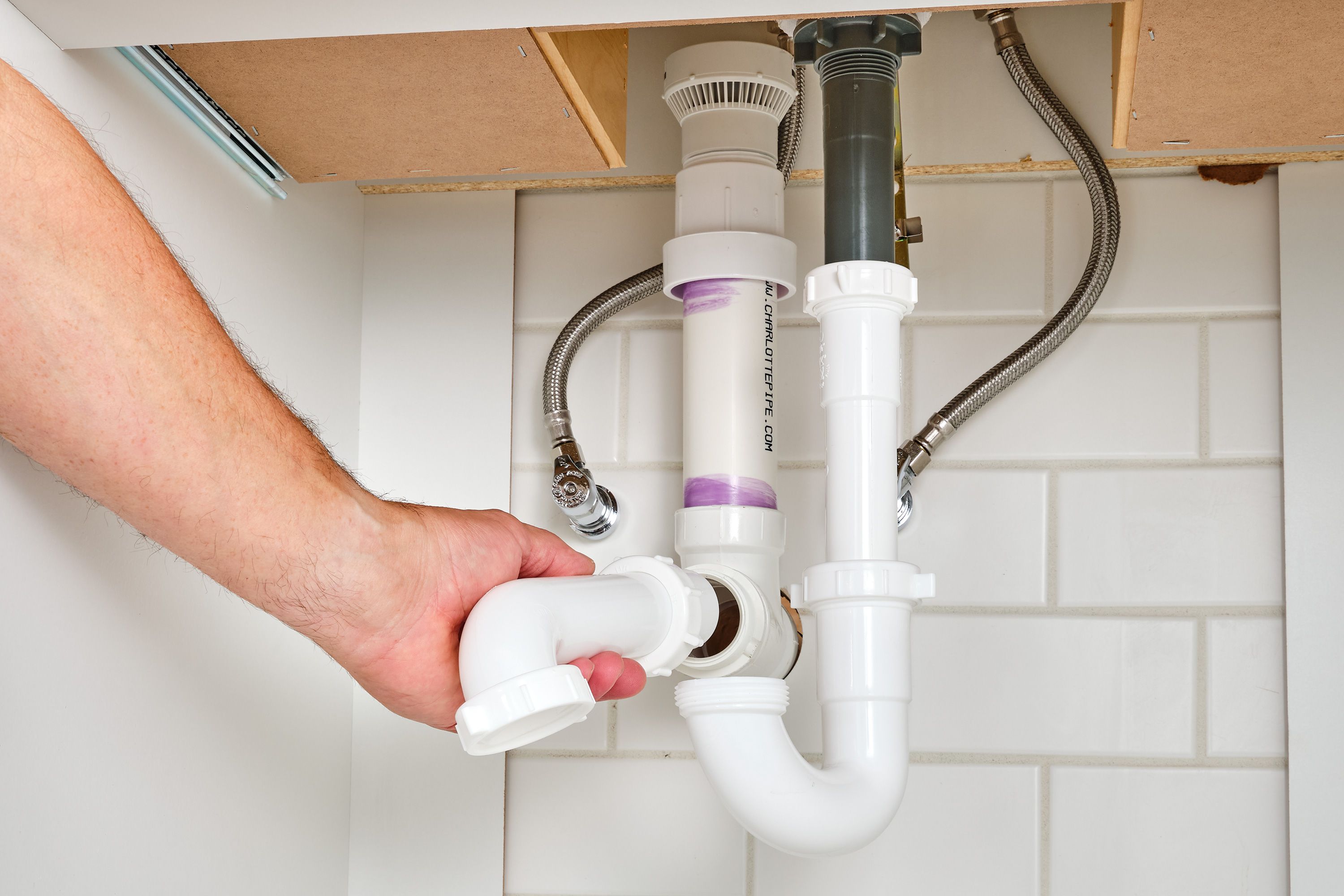 A photo inside a kitchen sink cabinet showing an air-admittance valve mounted upright on a vertical drain pipe near the back wall