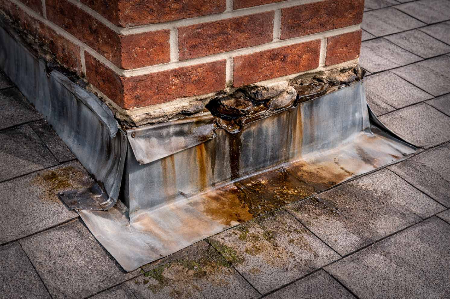 A photo inside an attic showing dark water staining on wood sheathing near a chimney chase, suggesting a flashing leak