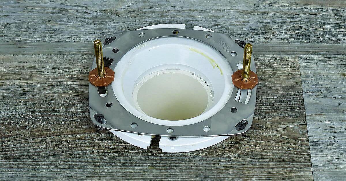 A photo of a stainless steel toilet flange repair ring being screwed down over an existing flange on a bathroom floor