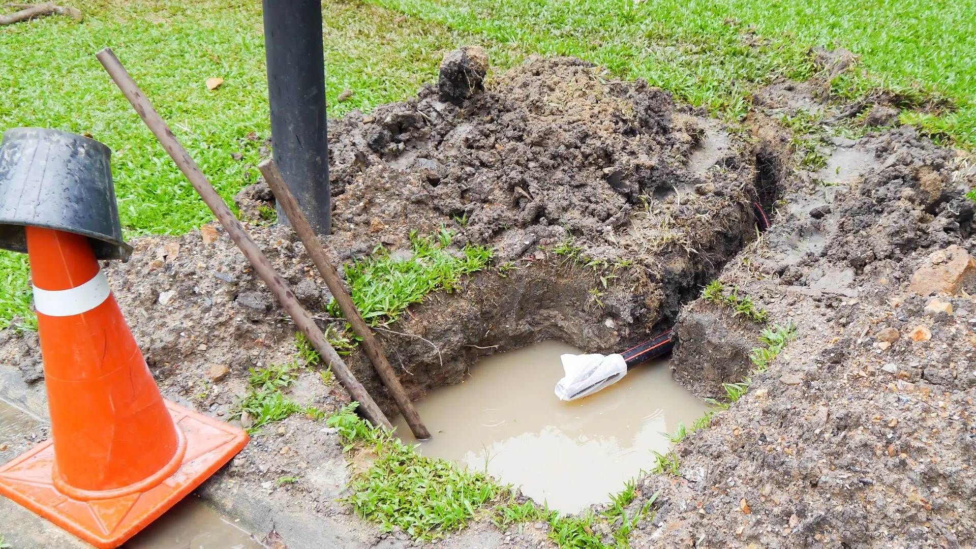 A photo of damp, sunken soil in a rural yard suggesting an underground water line leak near a well service trench