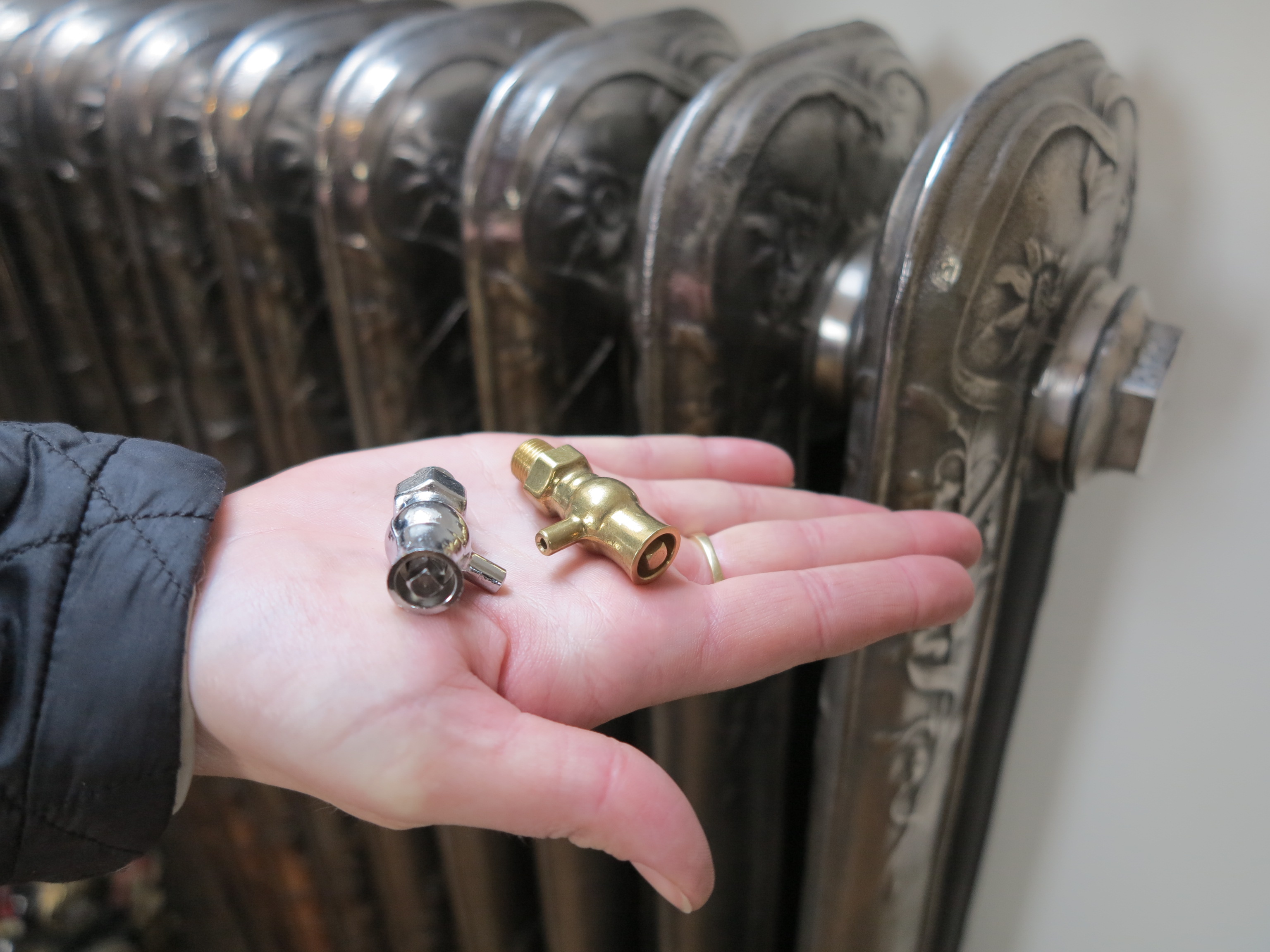 A photograph of a hand using a radiator key to bleed air from a cast iron radiator in an older home