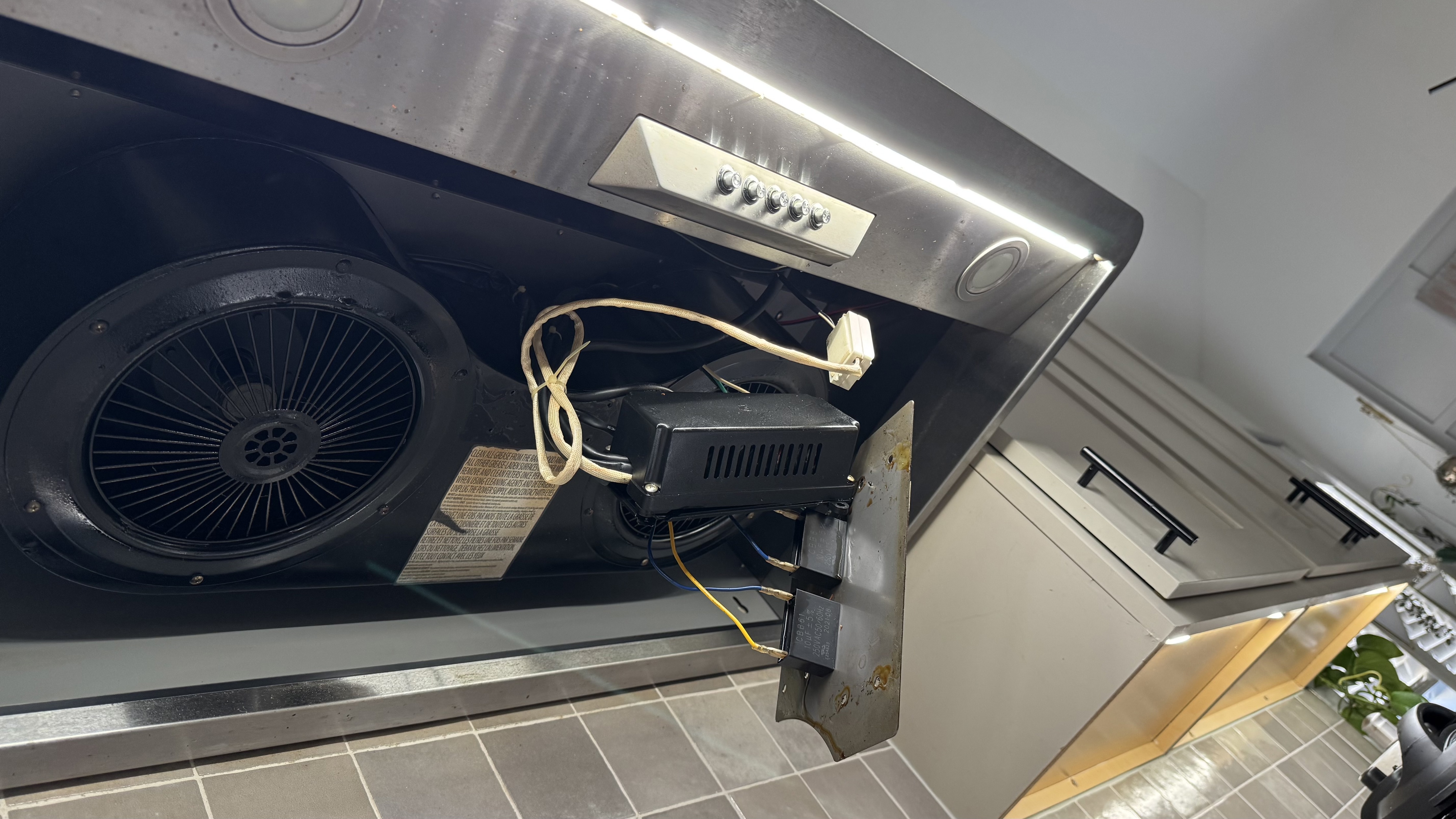 A photograph of the inside of a range hood with the filter removed, showing a small rectangular LED driver box mounted to the metal housing with wires connected