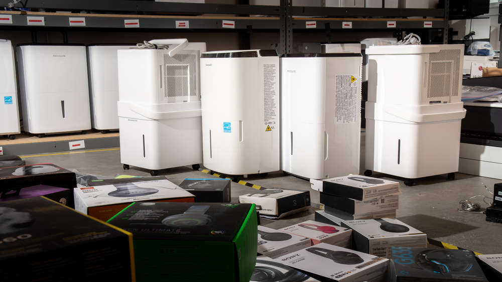 A portable dehumidifier running on a basement floor with the water bucket pulled out and visibly empty, natural indoor lighting, real photo
