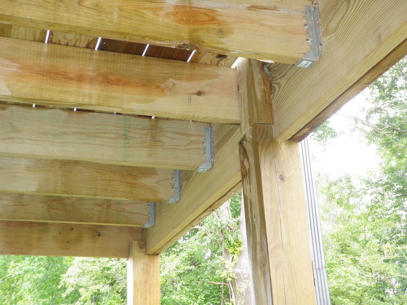 A pressure-treated double beam supported by vertical posts with metal post caps, photographed from underneath the deck