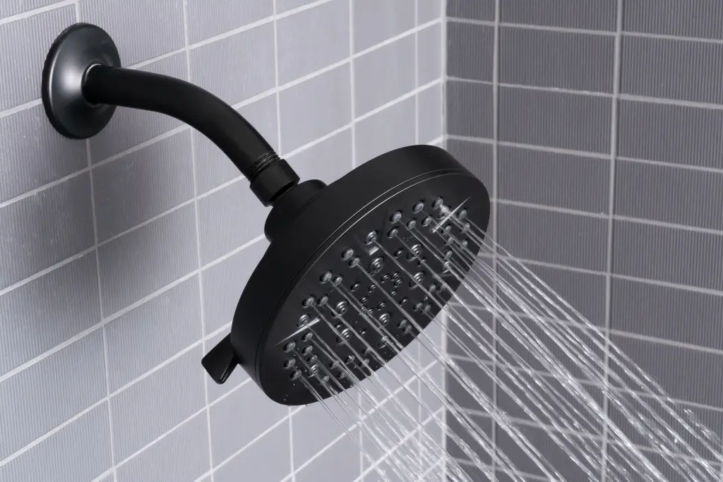 A real bathroom shower with water trickling weakly from a showerhead, with tile walls and a tub below, natural indoor lighting