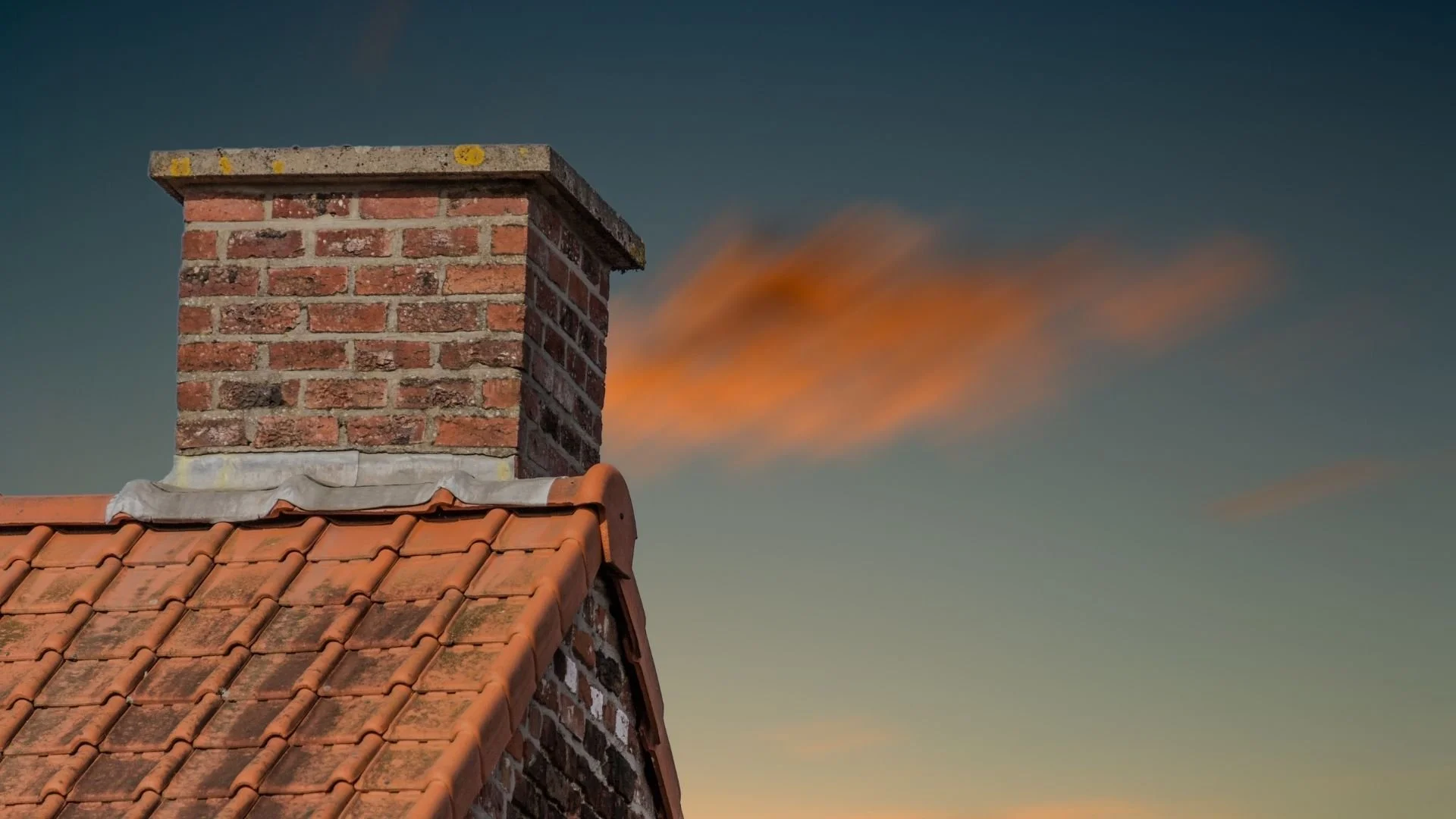 A real brick chimney with a metal chimney cap on top, photographed from the ground on a clear winter day, no text or labels
