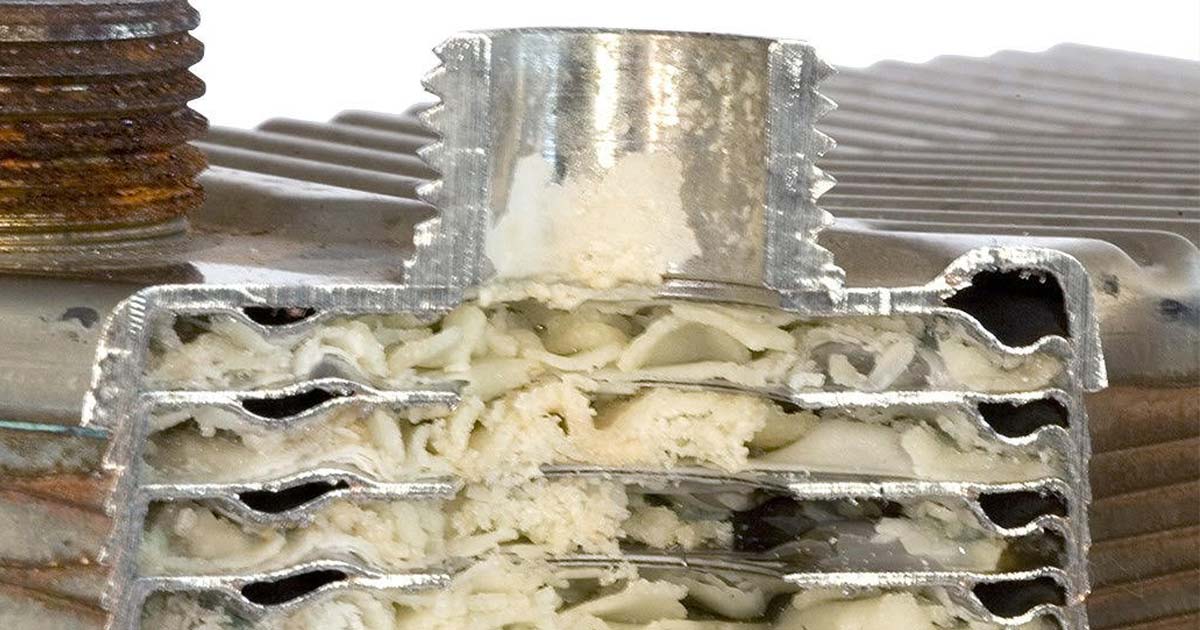 A real close-up photo of a boiler heat exchanger surface showing whitish mineral scale buildup during service