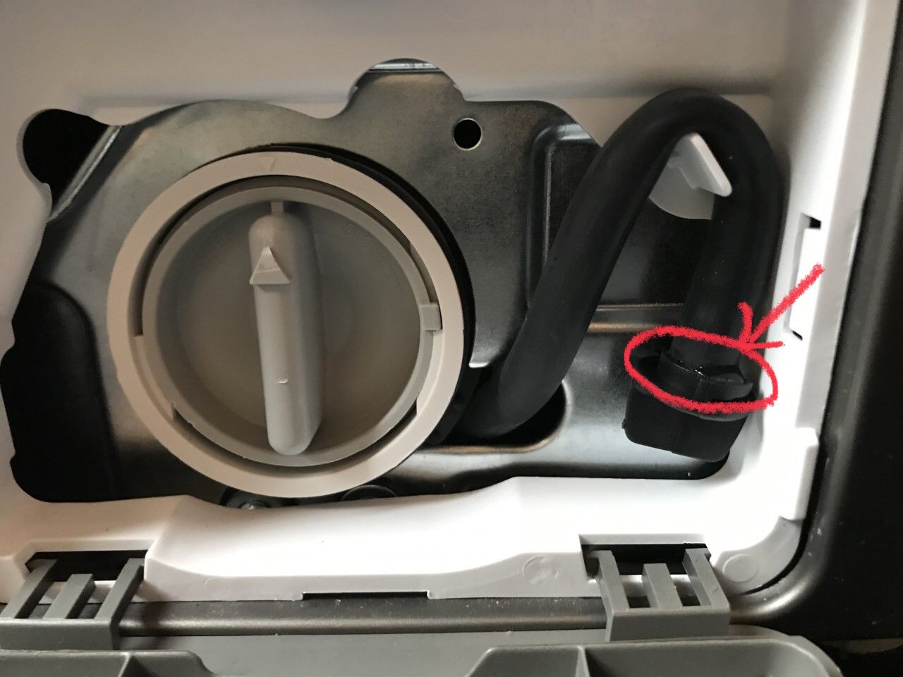A real close-up photo of a front-load washer emergency drain hose being held over a shallow pan with towels surrounding the area
