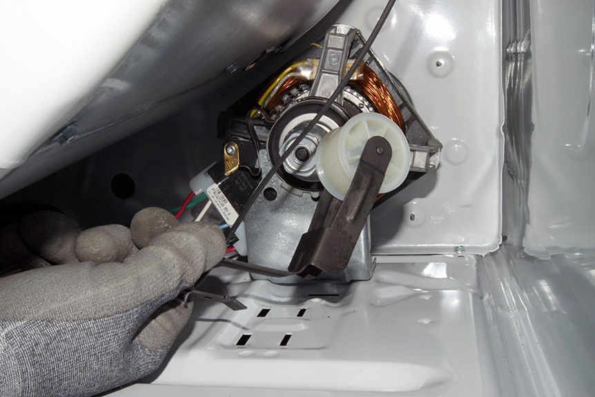A real close-up photo of an idler pulley mounted inside an open dryer cabinet, with the belt looped around it, indoor lighting, clear focus on the pulley wheel