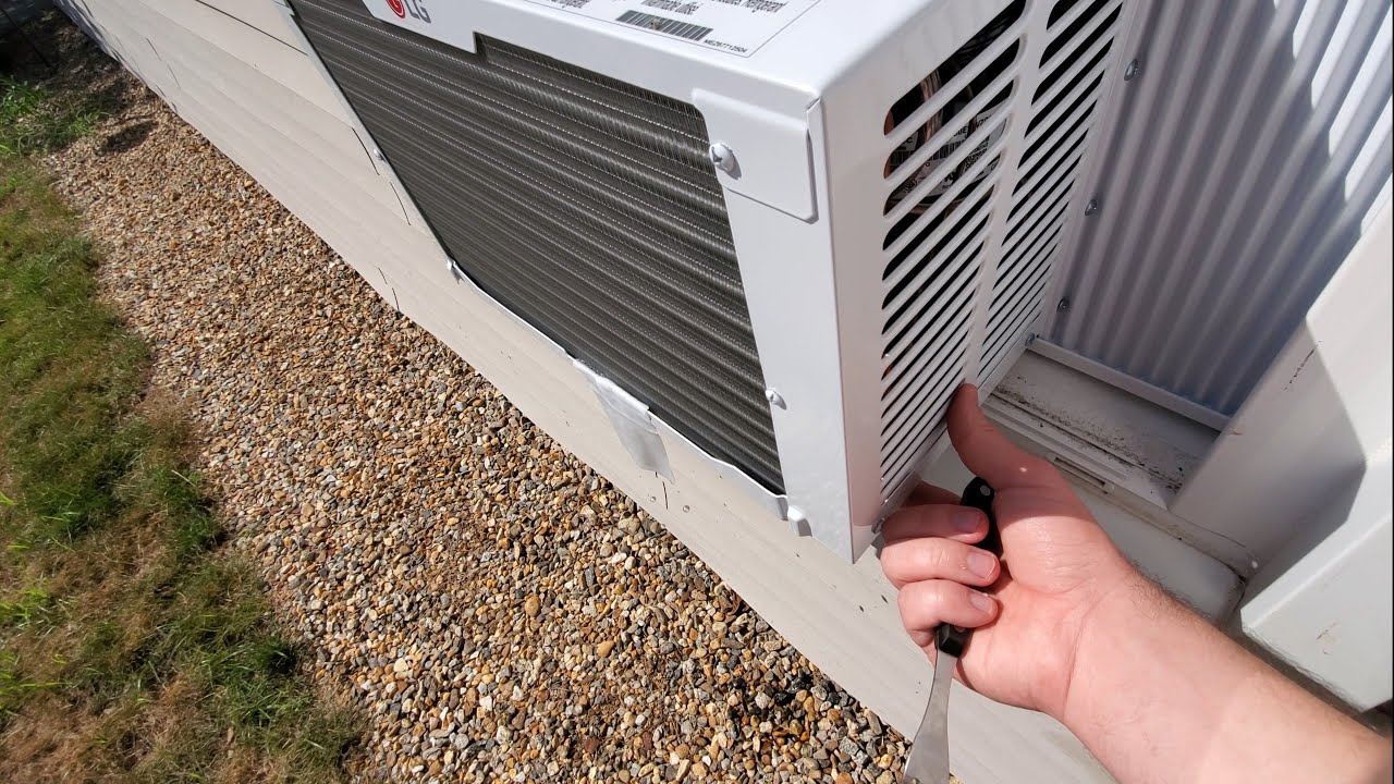 A real exterior view of a window air conditioner protruding outside, showing the back of the unit and the lower base area where water would normally drain