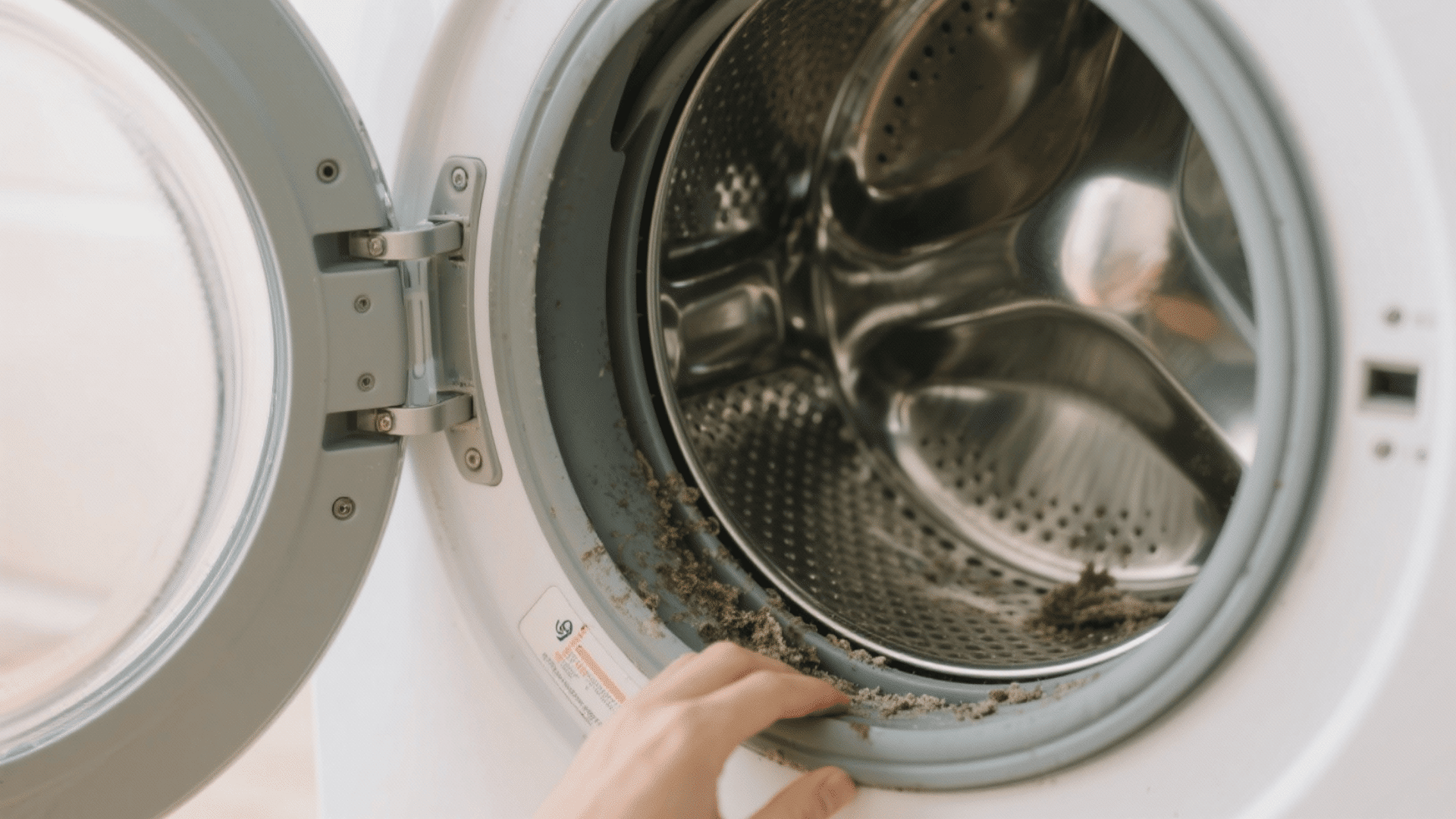 A real front-loading washer mid-cycle with visible suds clinging to the stainless drum and glass door, indoor laundry room photo