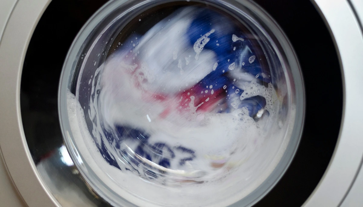 A real front-loading washing machine with a dark shirt draped over the door showing faint white detergent streaks after washing, natural indoor lighting