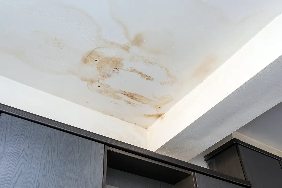 A real home interior ceiling with a skylight, showing a faint brown water stain and bubbling paint near the skylight frame on drywall
