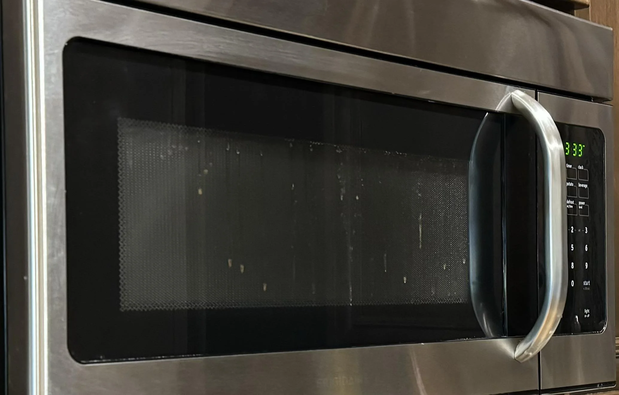 A real kitchen oven with visible fog and water droplets trapped between the oven door glass panes, shot straight on in natural indoor light