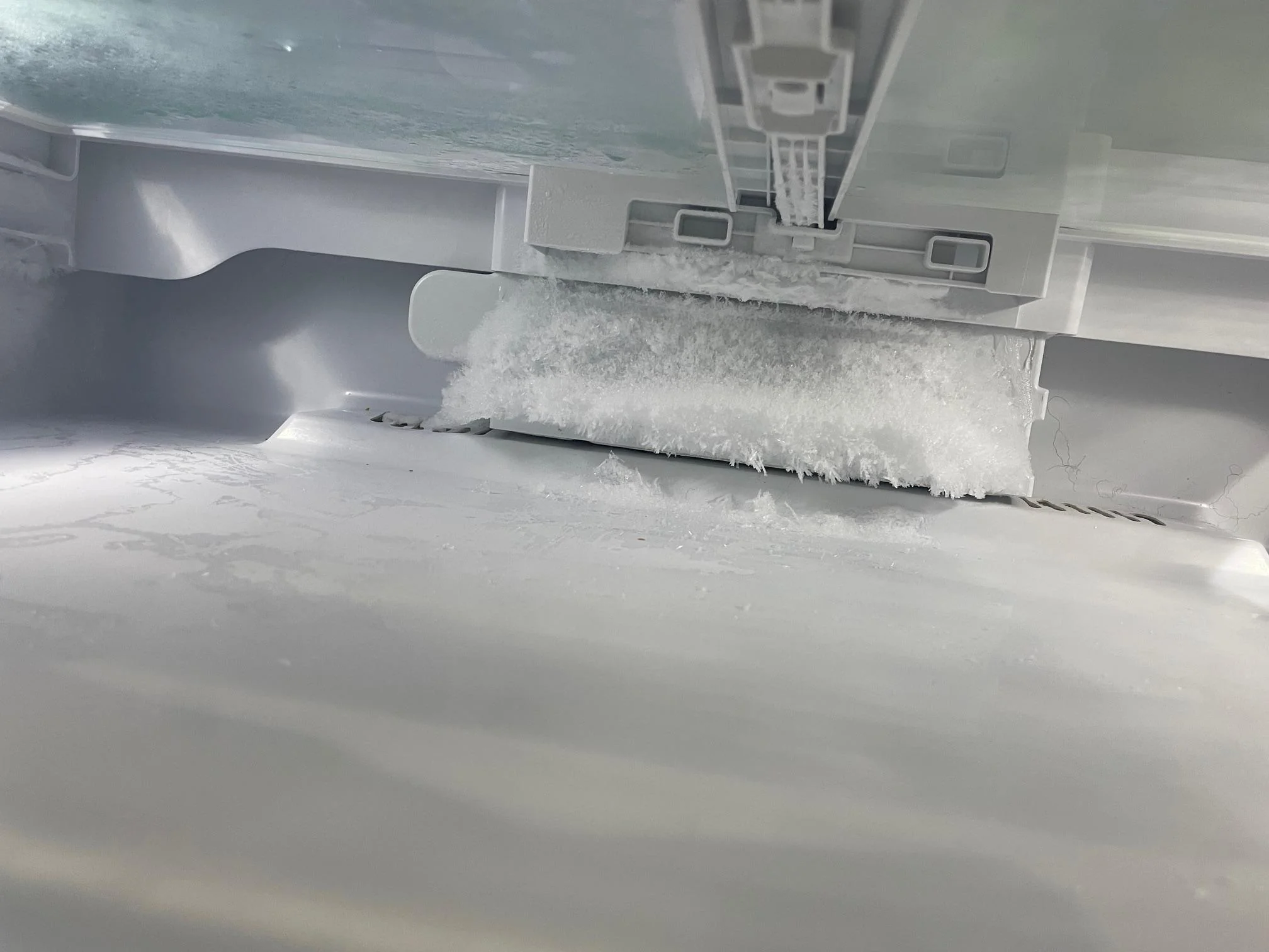A real kitchen refrigerator with the crisper drawers removed, showing a sheet of ice built up on the bottom floor of the fresh food compartment