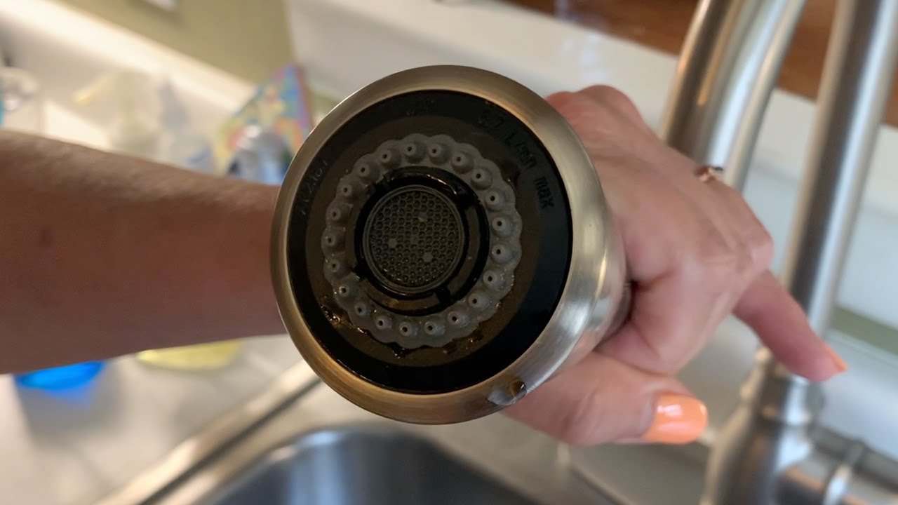 A real kitchen sprayer head sitting in a small bowl of white vinegar on a countertop, photographed close up with natural light