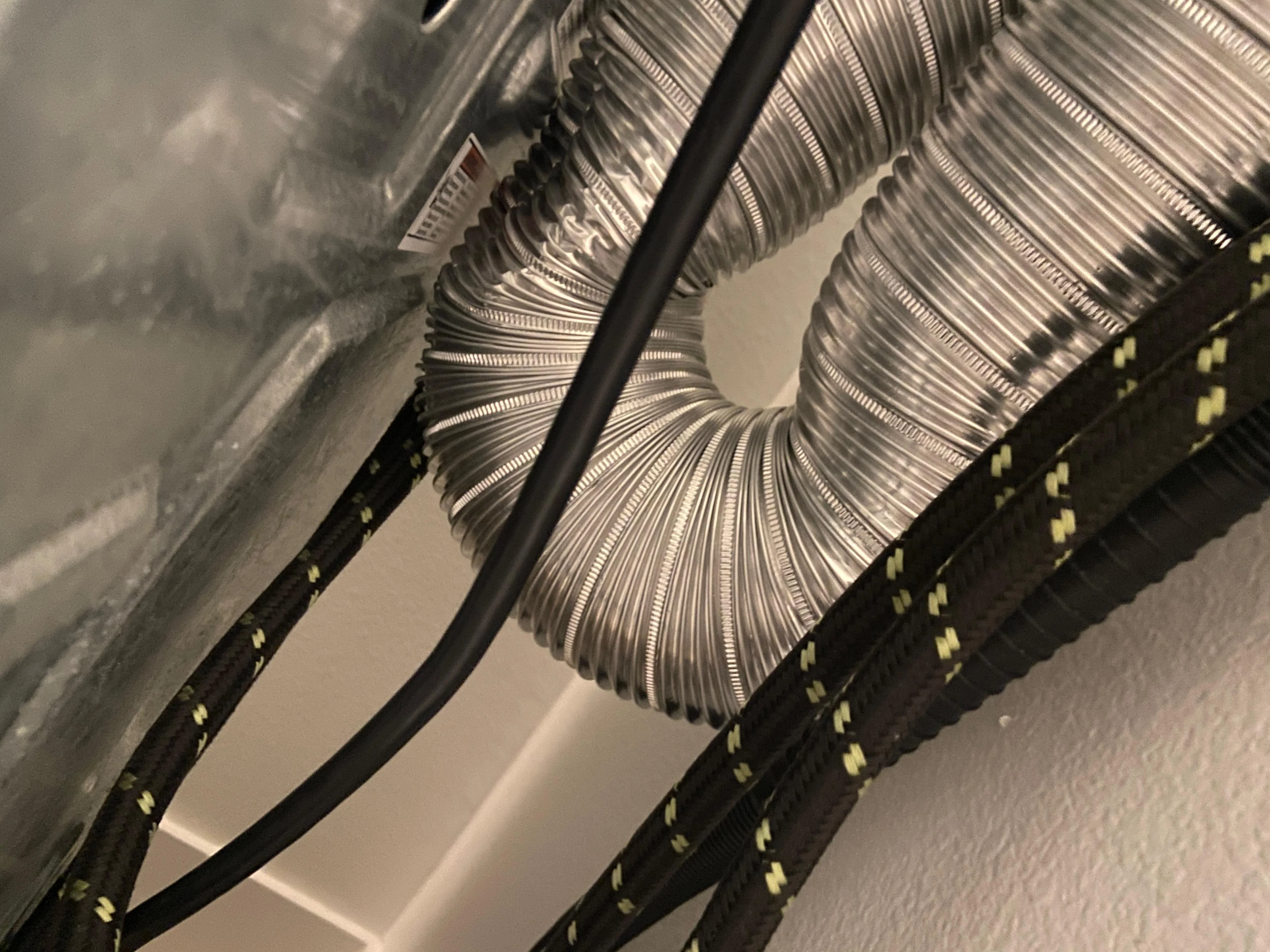 A real laundry room photo showing a dryer pulled forward with a kinked silver flexible vent hose pressed against the wall