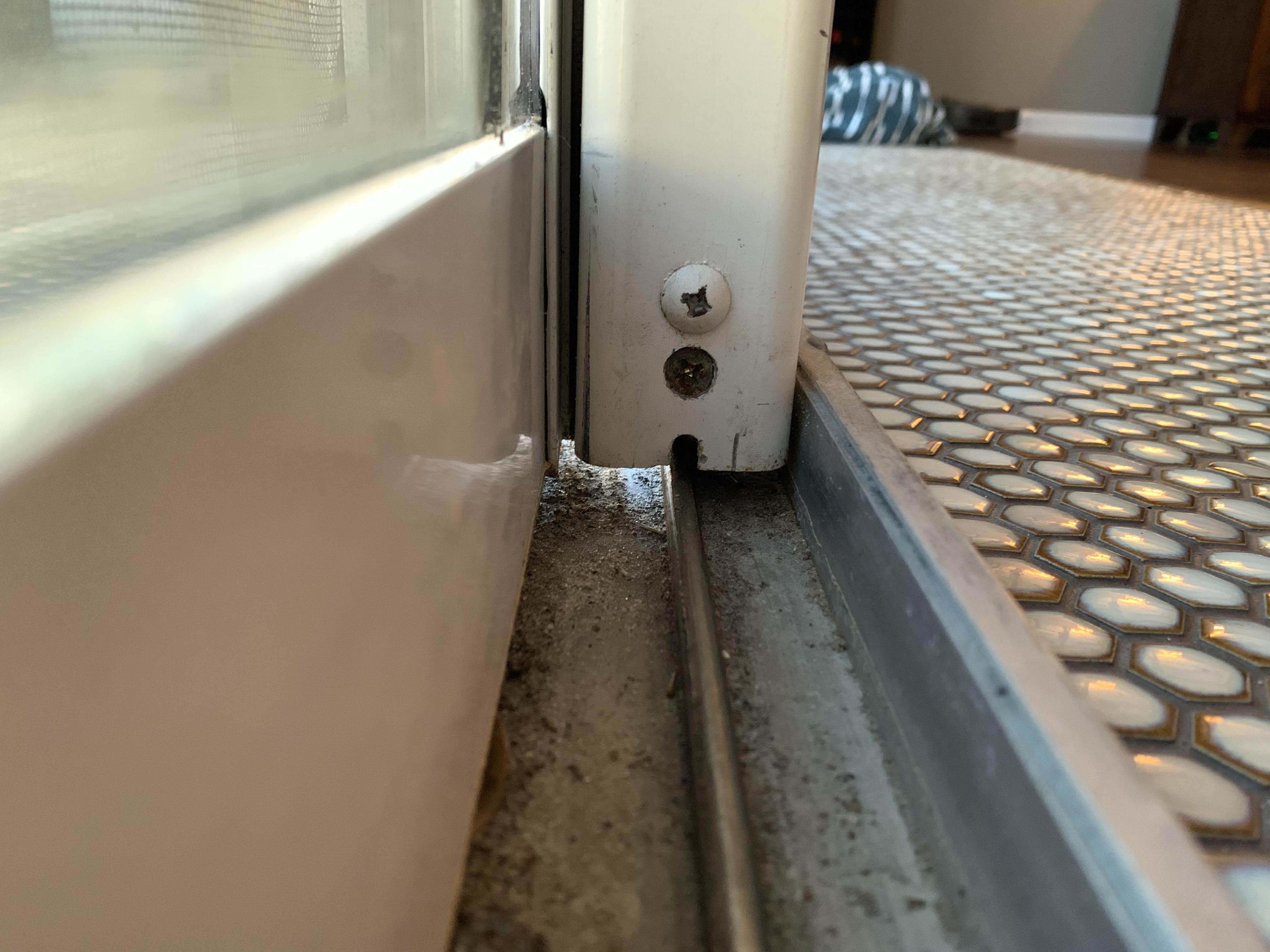 A real photo close-up of a worn sliding patio door track showing a visible groove near the jamb where the rollers repeatedly pass