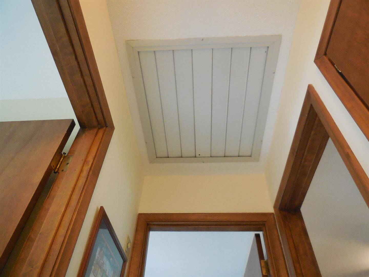 A real photo closeup of white louvered shutters on a whole-house fan grille, partially open with visible hinge points