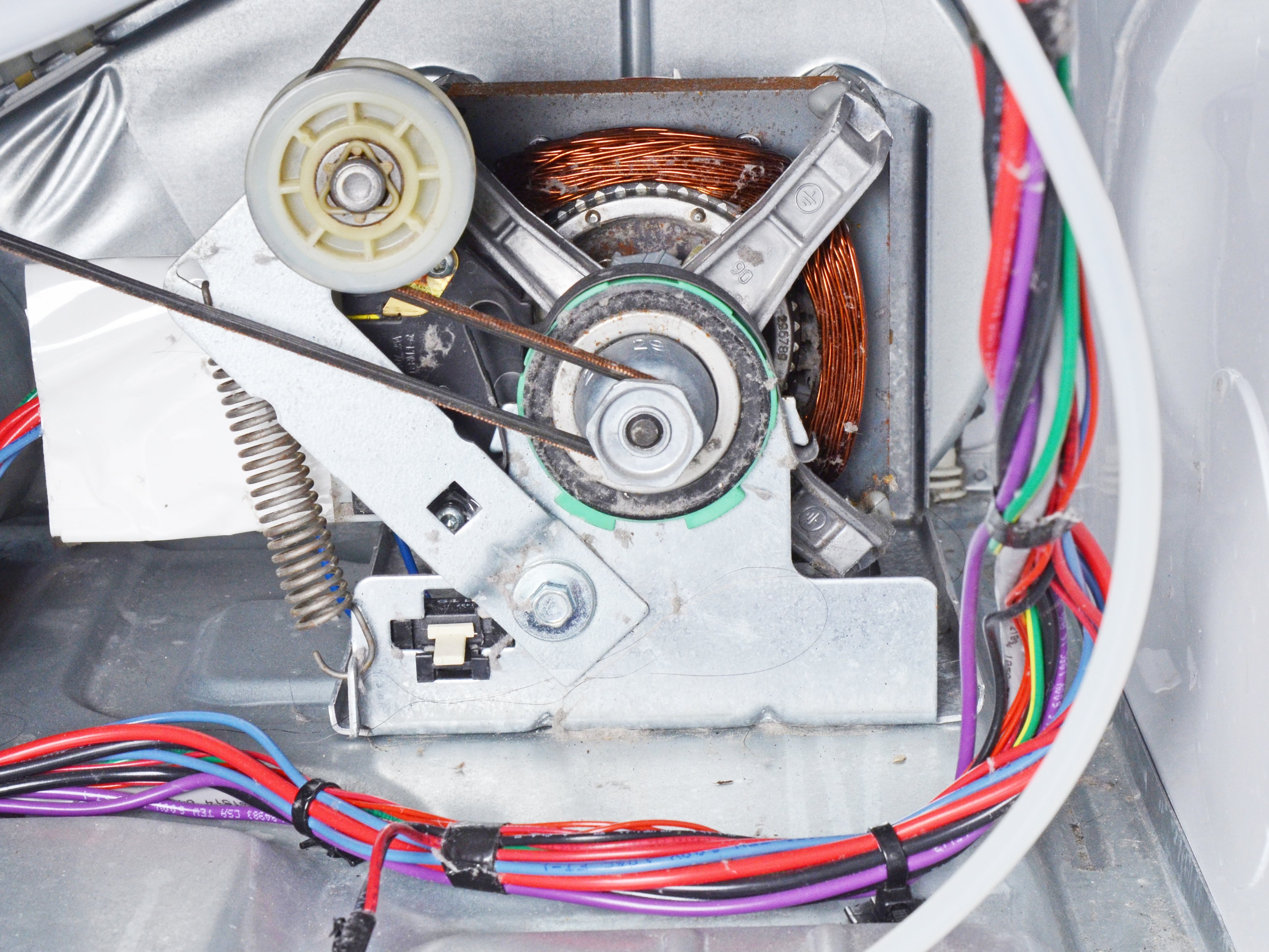 A real photo inside a dryer cabinet showing the belt routed around the motor pulley and idler pulley, with the belt taut and properly seated