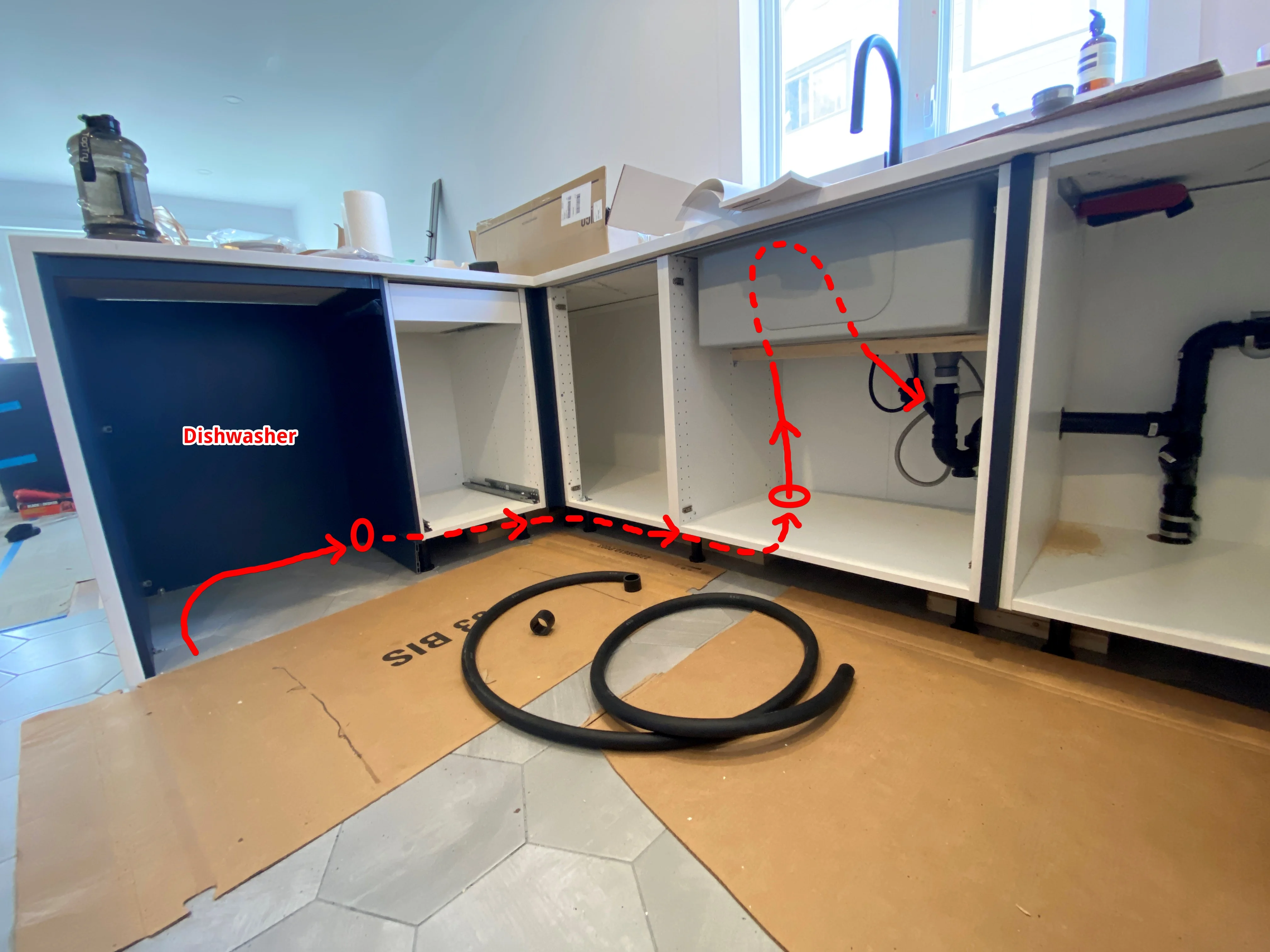 A real photo inside a kitchen sink cabinet showing the dishwasher drain hose fastened to the underside of the countertop with a metal strap