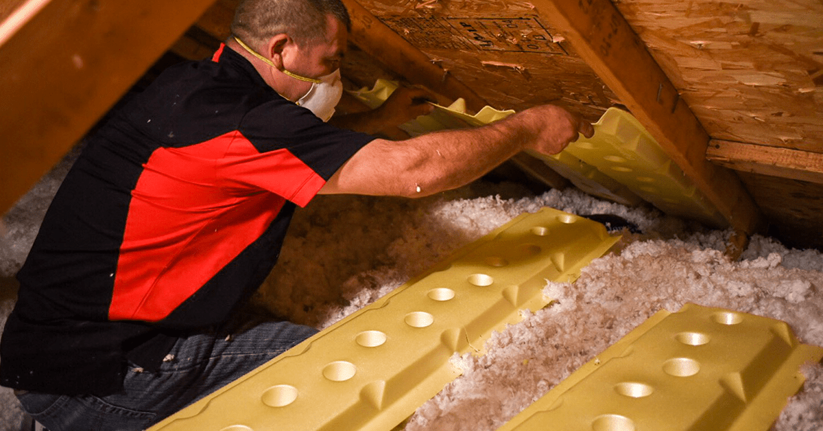 A real photo inside an attic showing insulation on the attic floor and plastic baffles installed at the eaves to keep soffit airflow clear