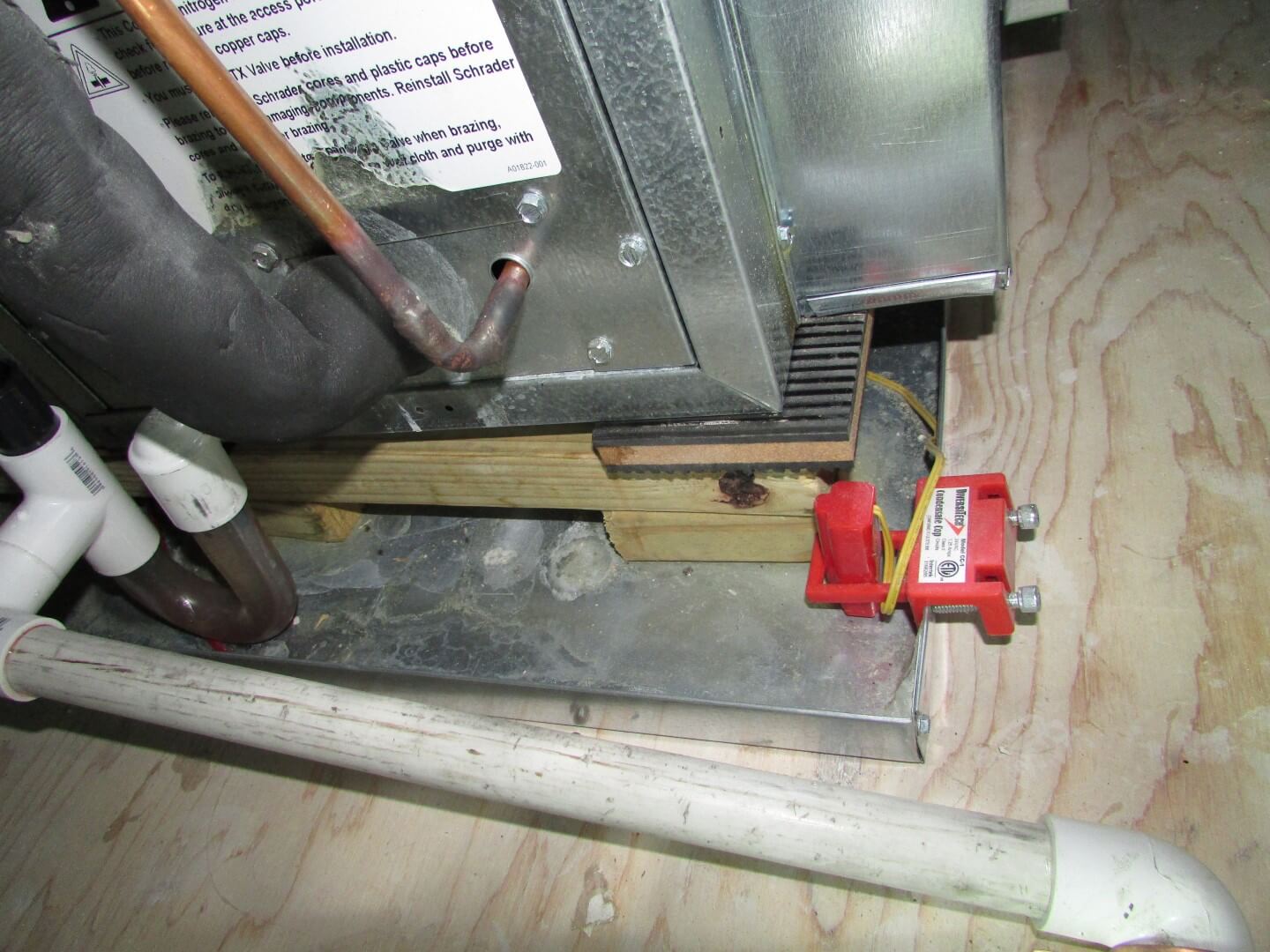 A real photo of a PVC HVAC condensate drain line with a capped cleanout tee next to an attic air handler