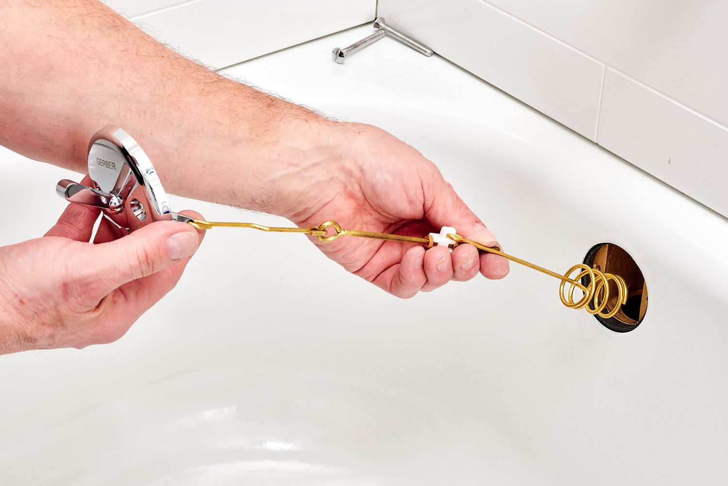 A real photo of a bathtub overflow plate being pulled away from the tub with a long metal linkage and plunger assembly extending out