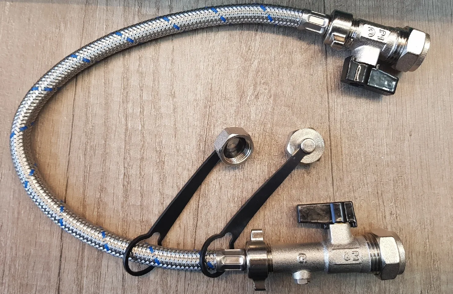 A real photo of a combi boiler’s braided metal filling loop hose with two small quarter-turn valves beneath the boiler