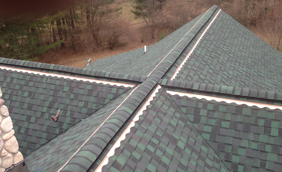 A real photo of a copper strip installed just below the ridge cap on an asphalt shingle roof, secured neatly and lying flat