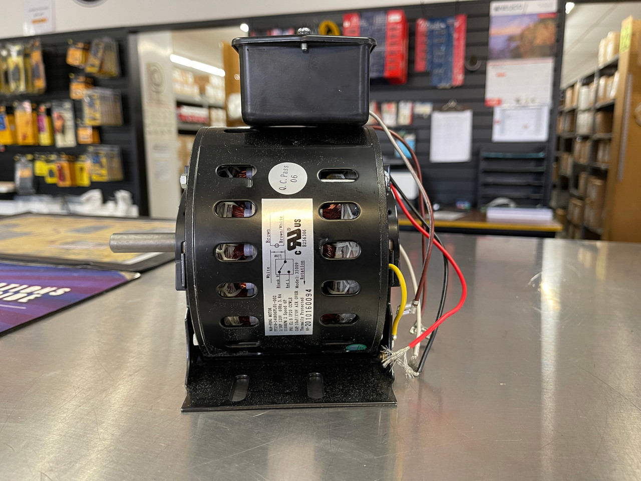 A real photo of a cylindrical motor capacitor strapped inside a whole-house attic fan housing next to the motor wiring