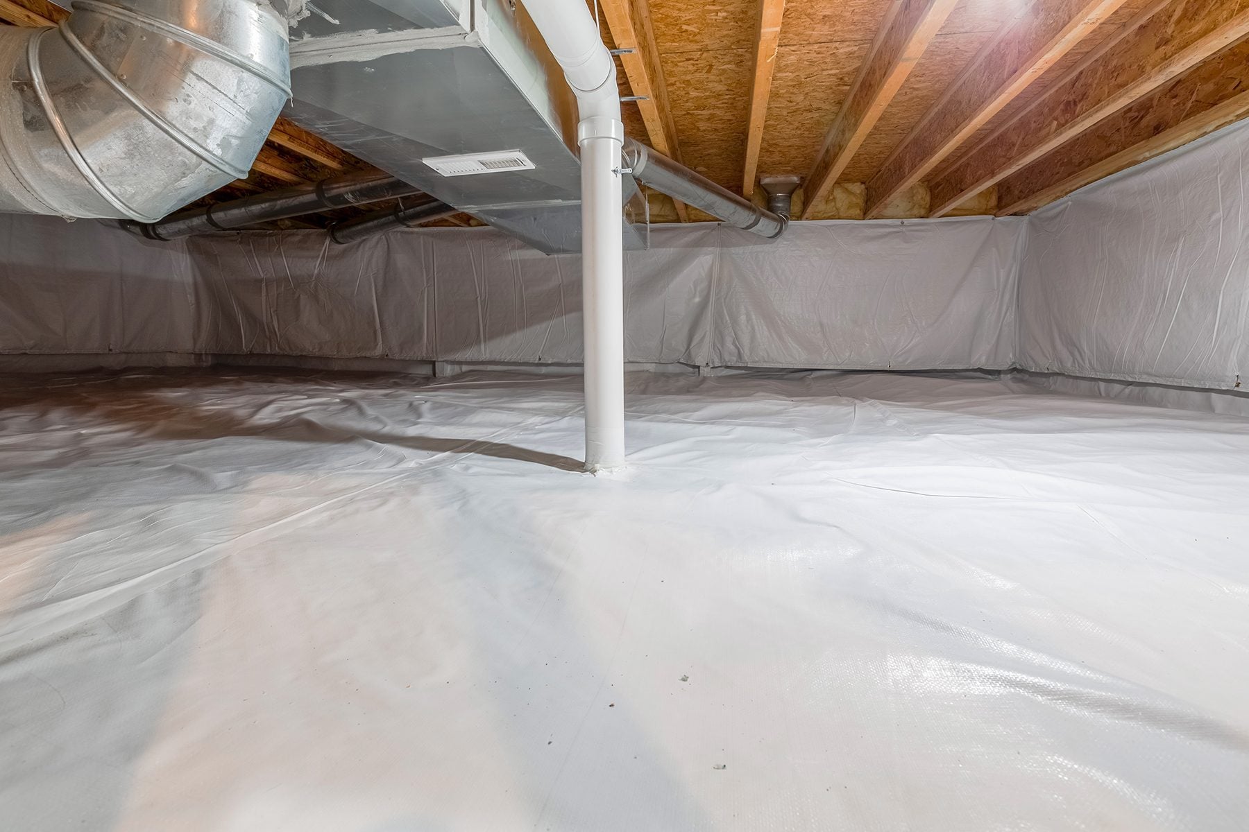 A real photo of a damp residential crawl space with exposed soil and scattered plastic sheeting, showing moisture-darkened ground and low clearance